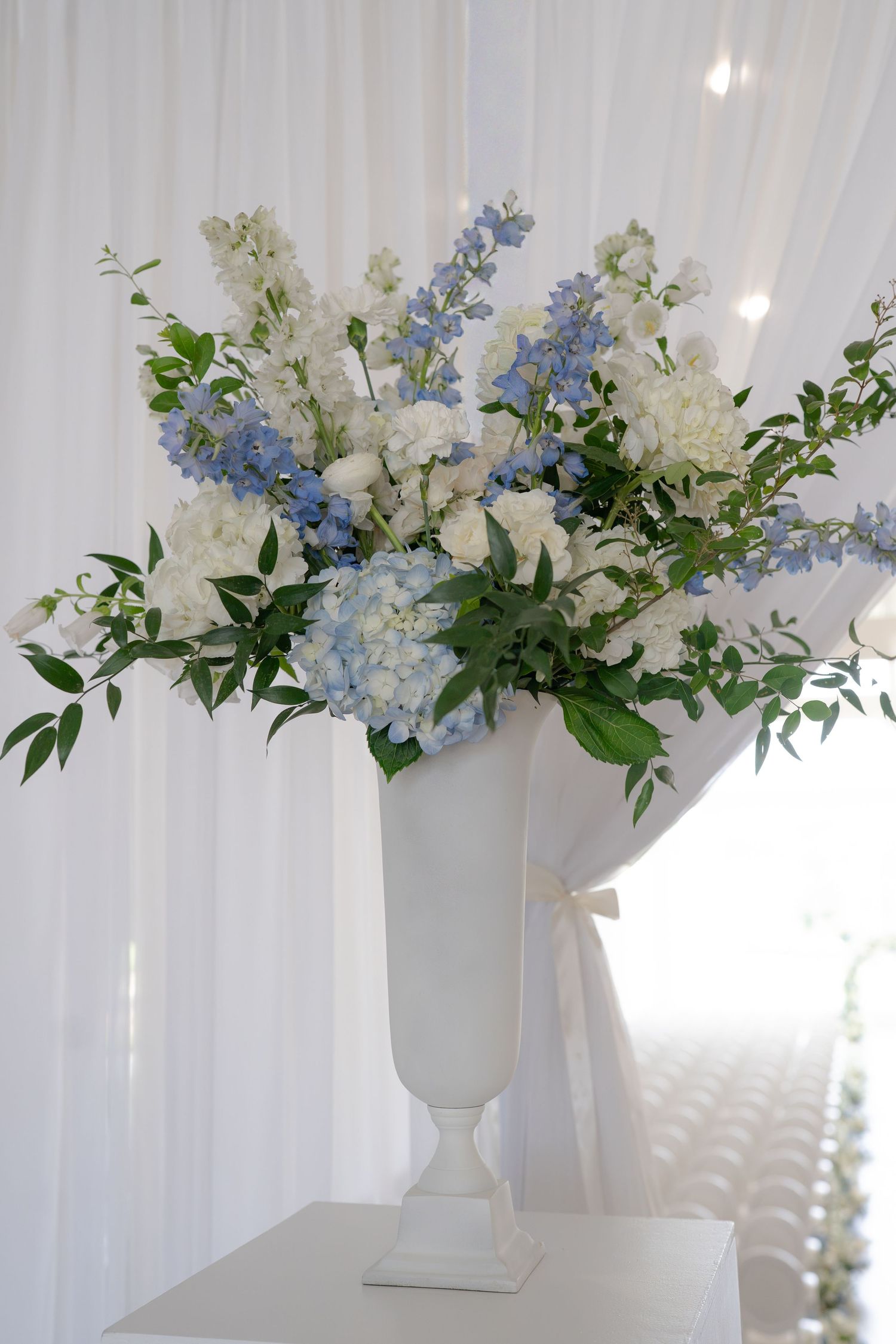 White vase with blue hydrangeas and white flowers arrangement at an elegant wedding ceremony venue.