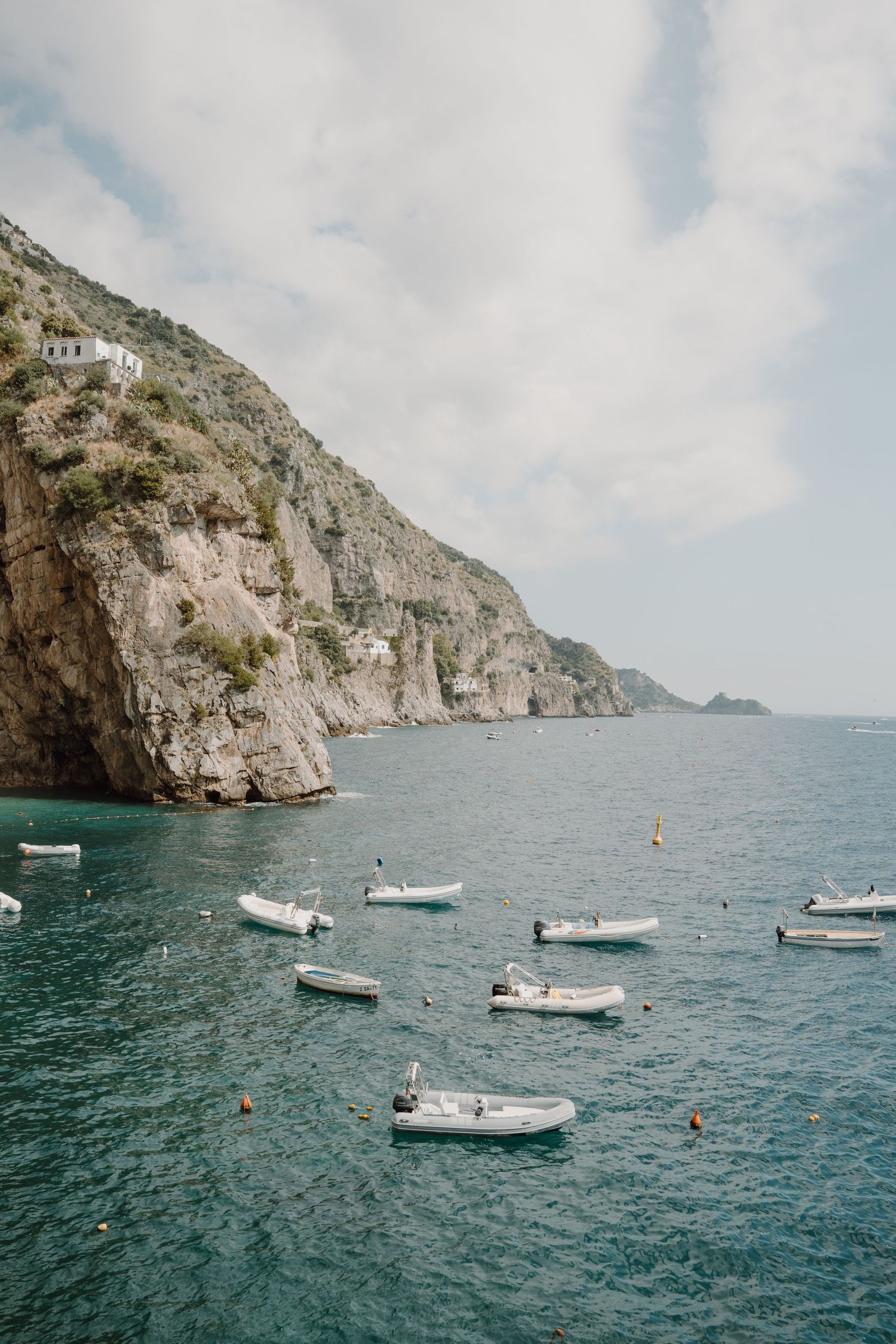 Scenic Mediterranean cove with white boats anchored near dramatic rocky cliffs.