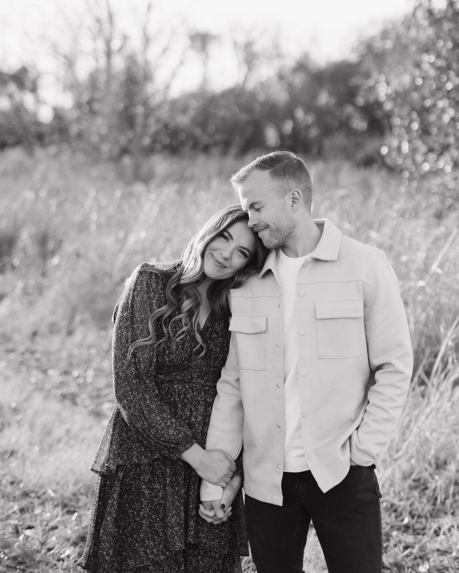 Black and white engagement photos of couple in casual attire posing in field.