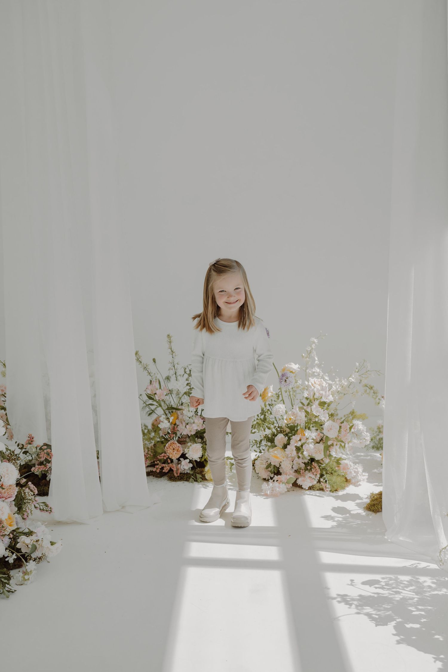 Ethereal white studio setup with delicate floral arrangements and soft natural lighting creating a dreamy atmosphere.