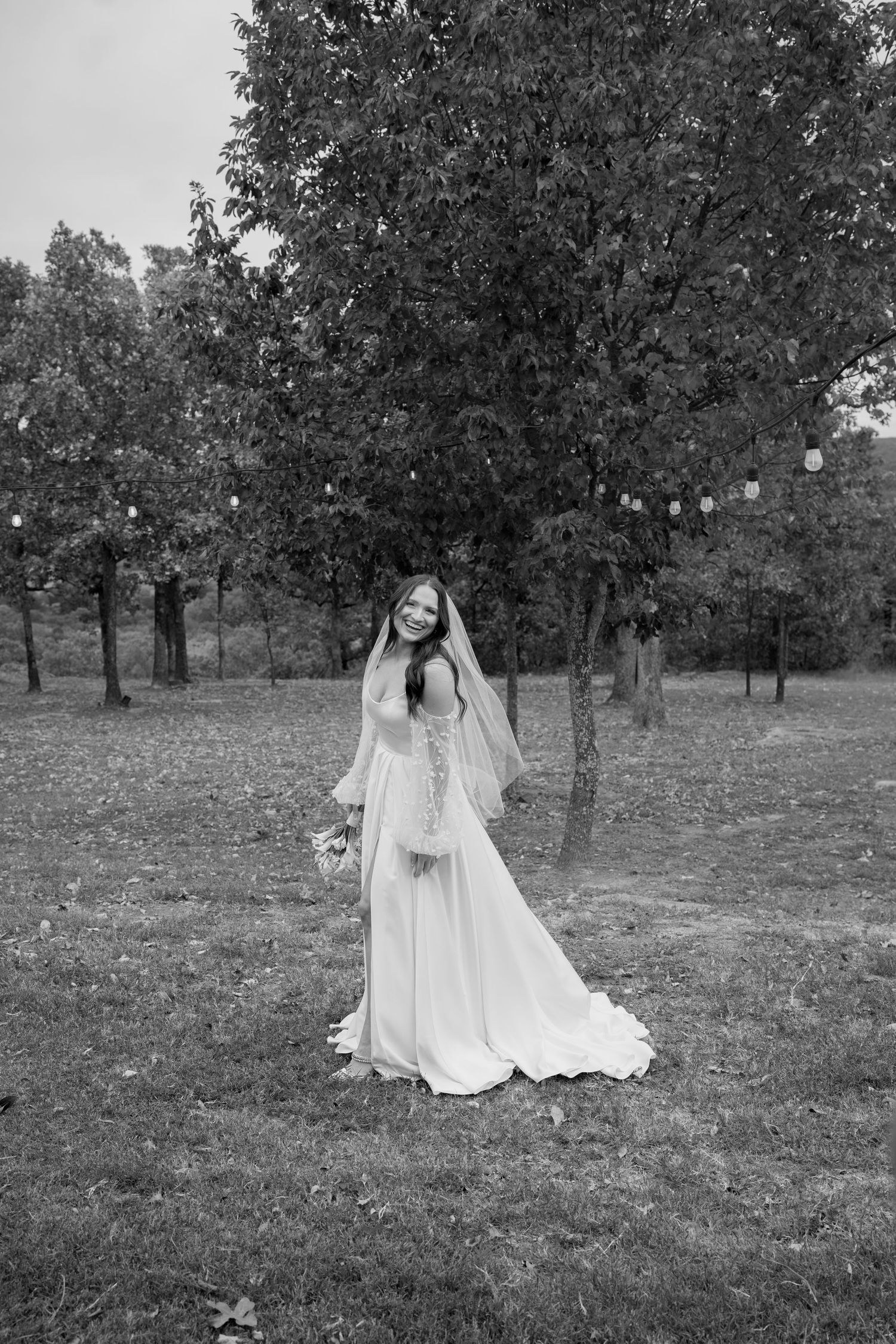 A black and white bridal portrait showing a flowing wedding dress in a garden setting.