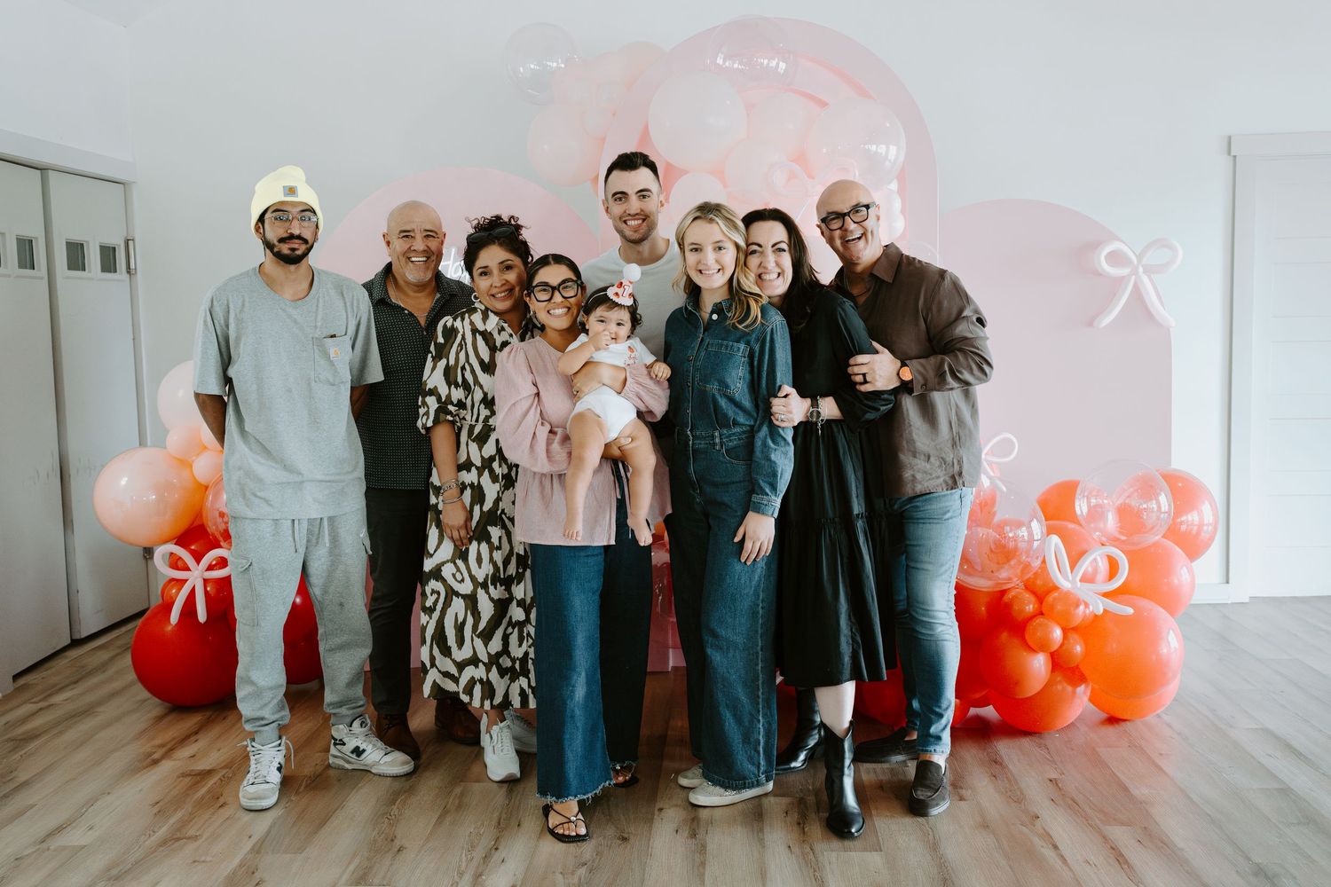 Large group portrait in front of a pink and orange balloon wall decoration.