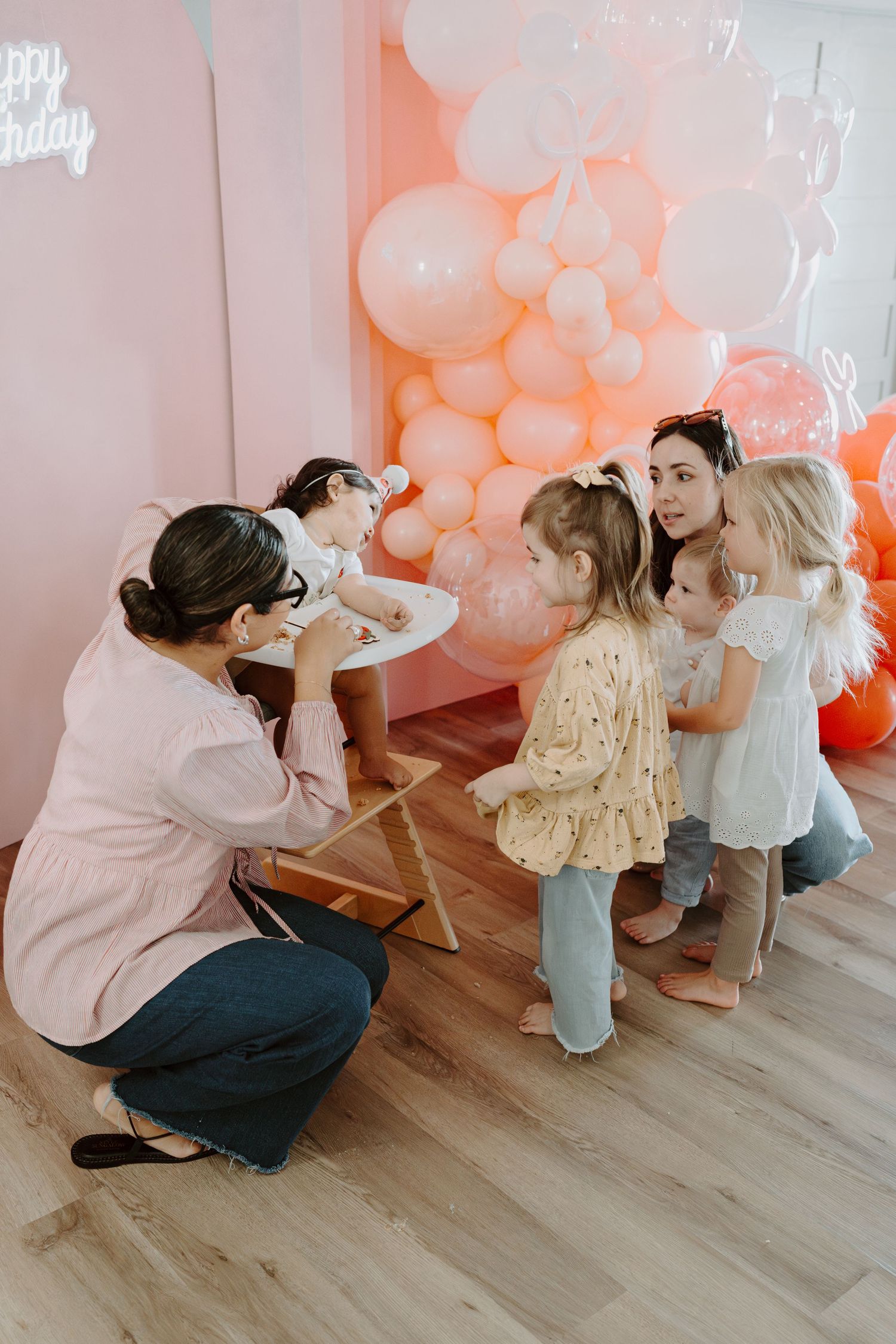 A series of candid shots showing playful interactions with a toddler in a room decorated with peach-colored balloons.