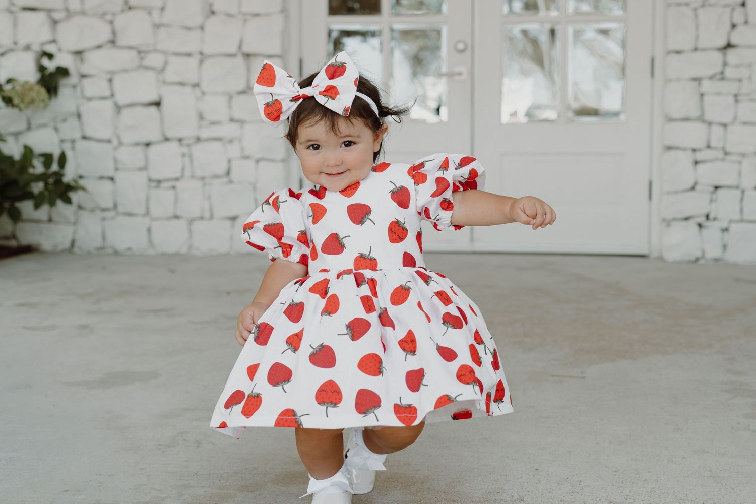 Cheerful pose in heart-print dress with matching bow against stone background.