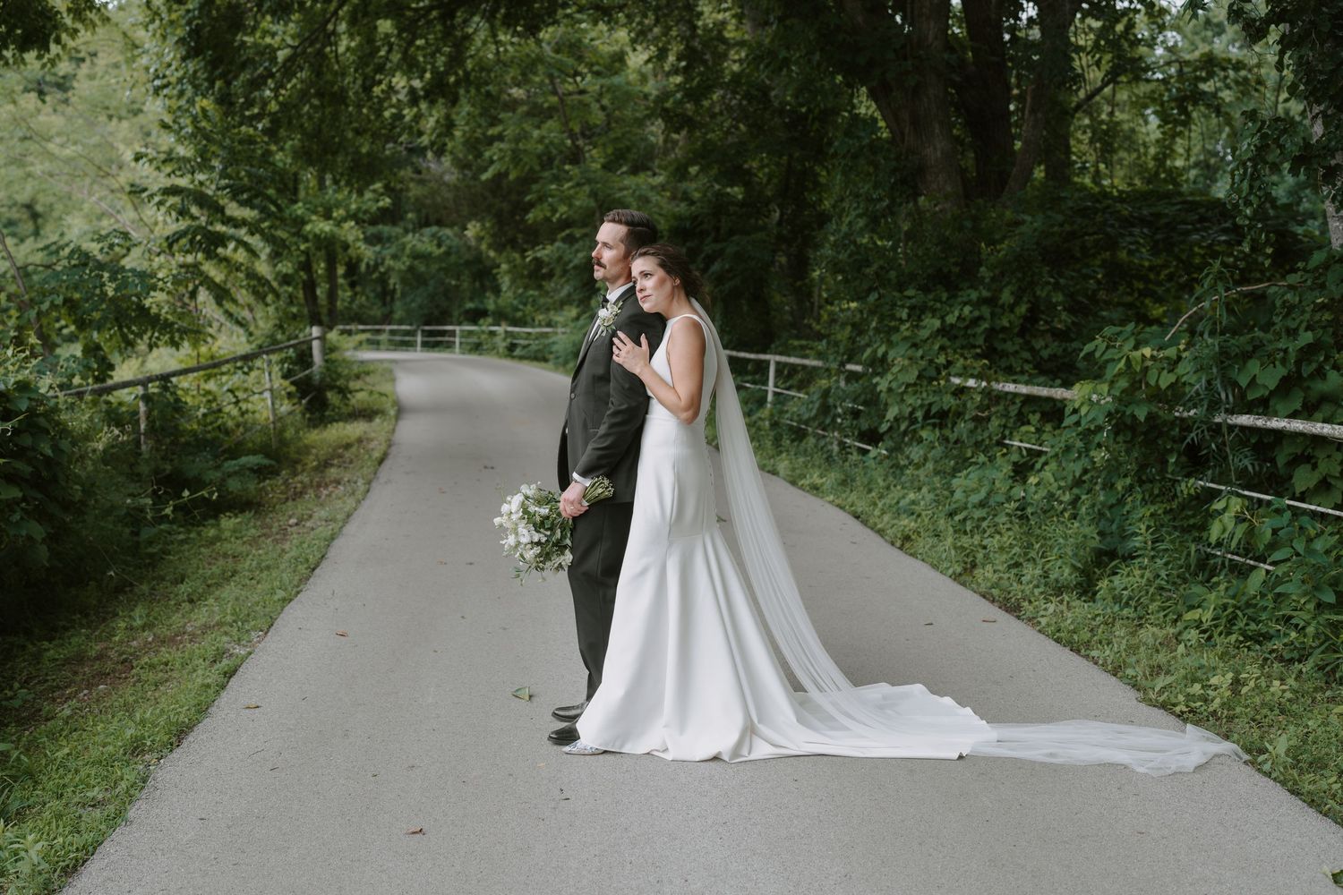 Scenic wedding portrait on a curved path surrounded by verdant forest landscape.