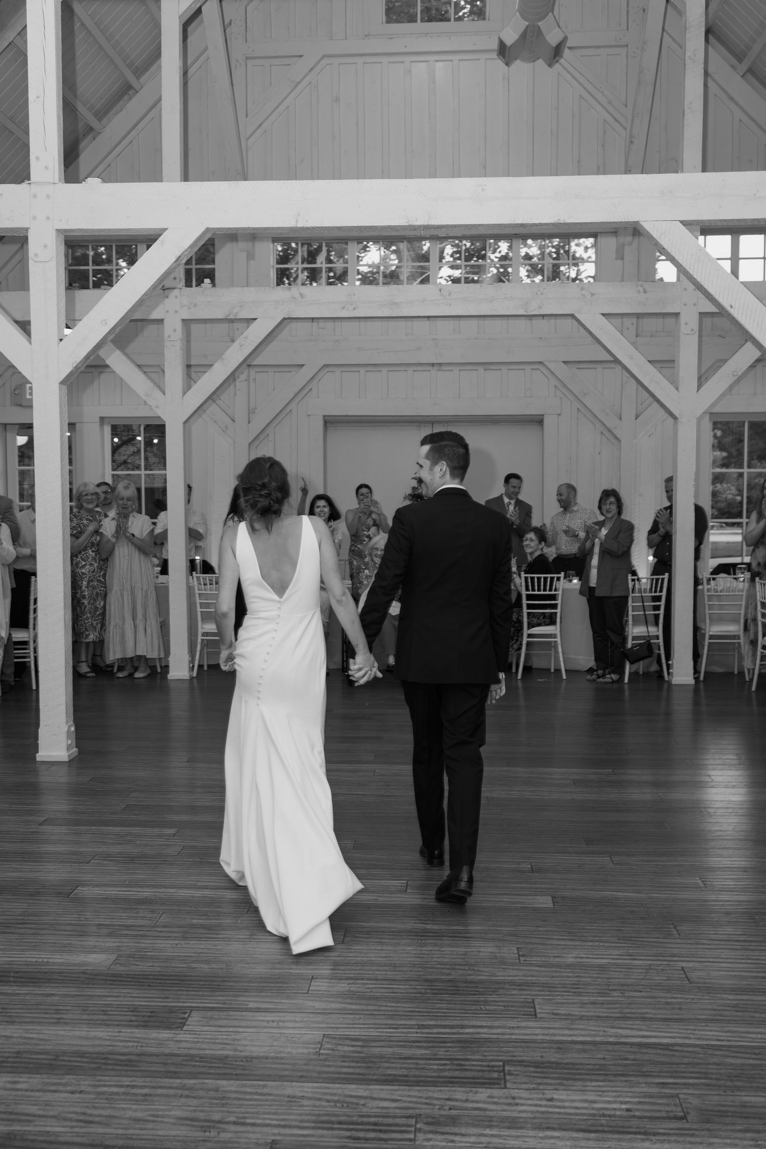 Couple performing first dance in a rustic white reception hall with guests watching from tables.