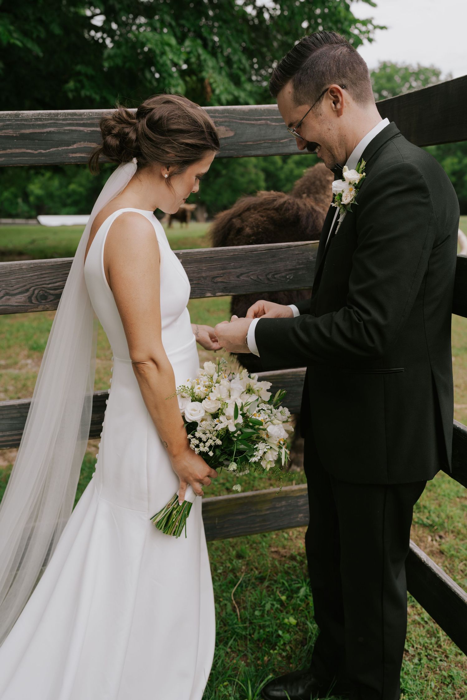 Wedding couple sharing an intimate moment by a rustic wooden fence during their countryside ceremony.
