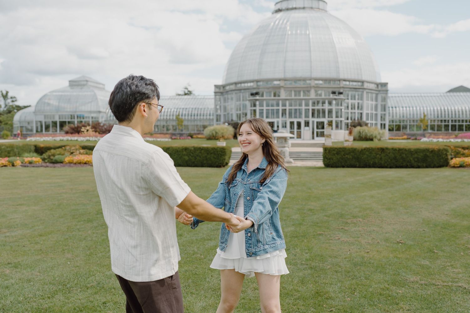 Couple dancing together on grass with a grand glass conservatory dome in the background.