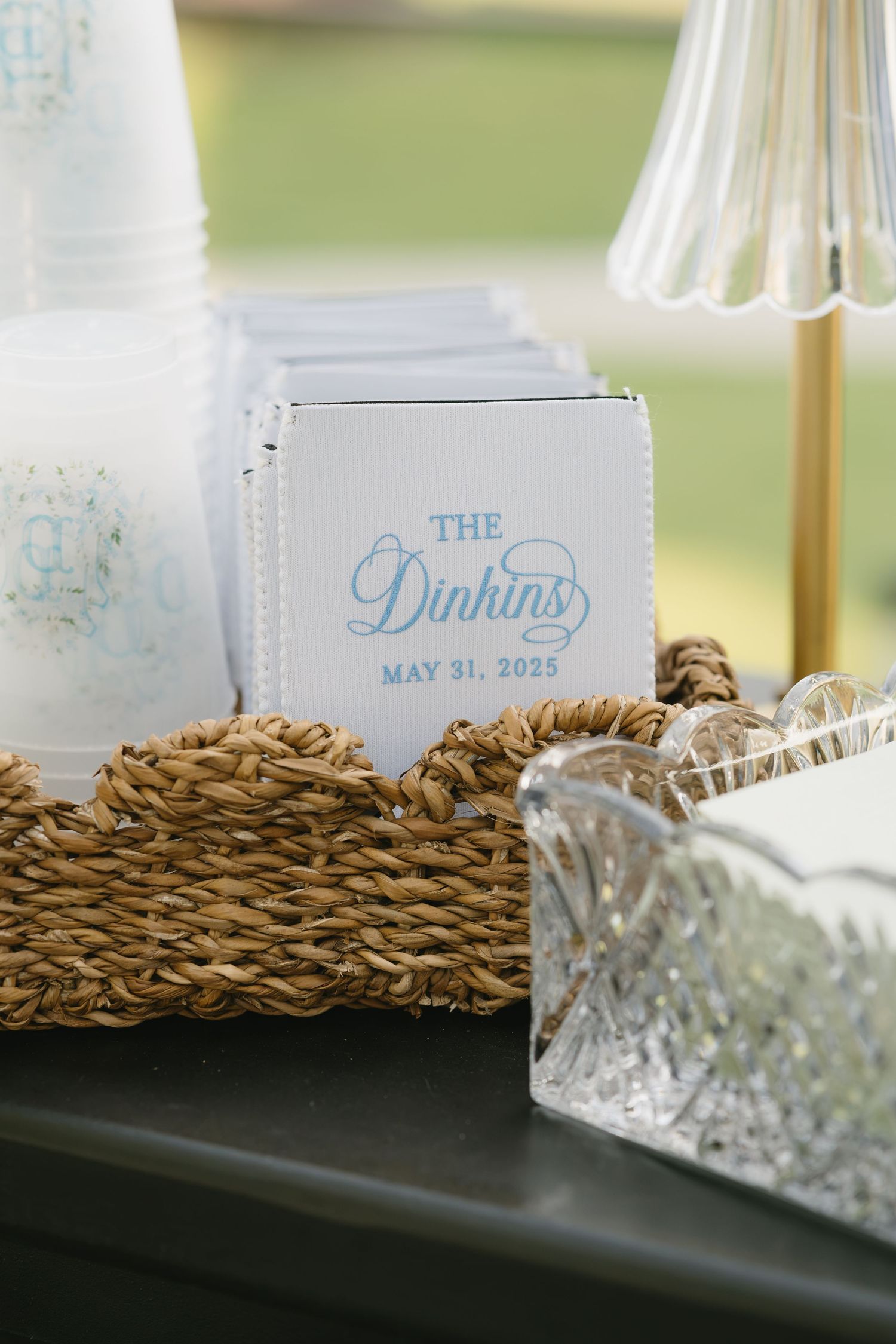 Custom white foam koozies printed with The Dinkins May 31, 2025 displayed in a wicker basket at a wedding reception.