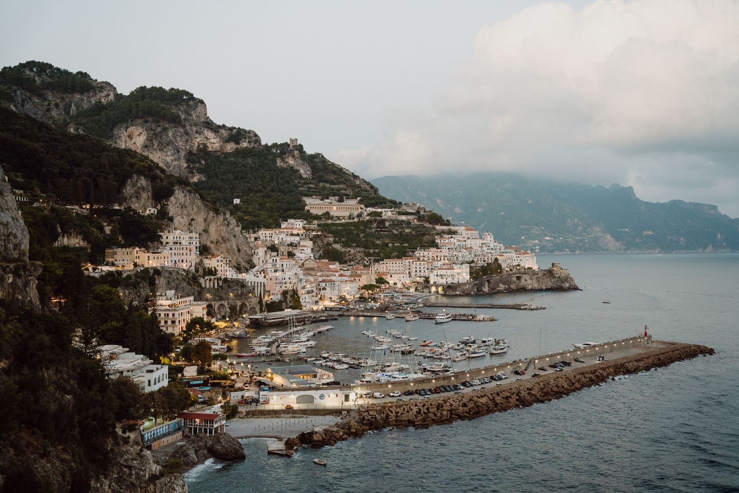 Coastal panorama of Positano harbor with boats and Mediterranean architecture along the shoreline.