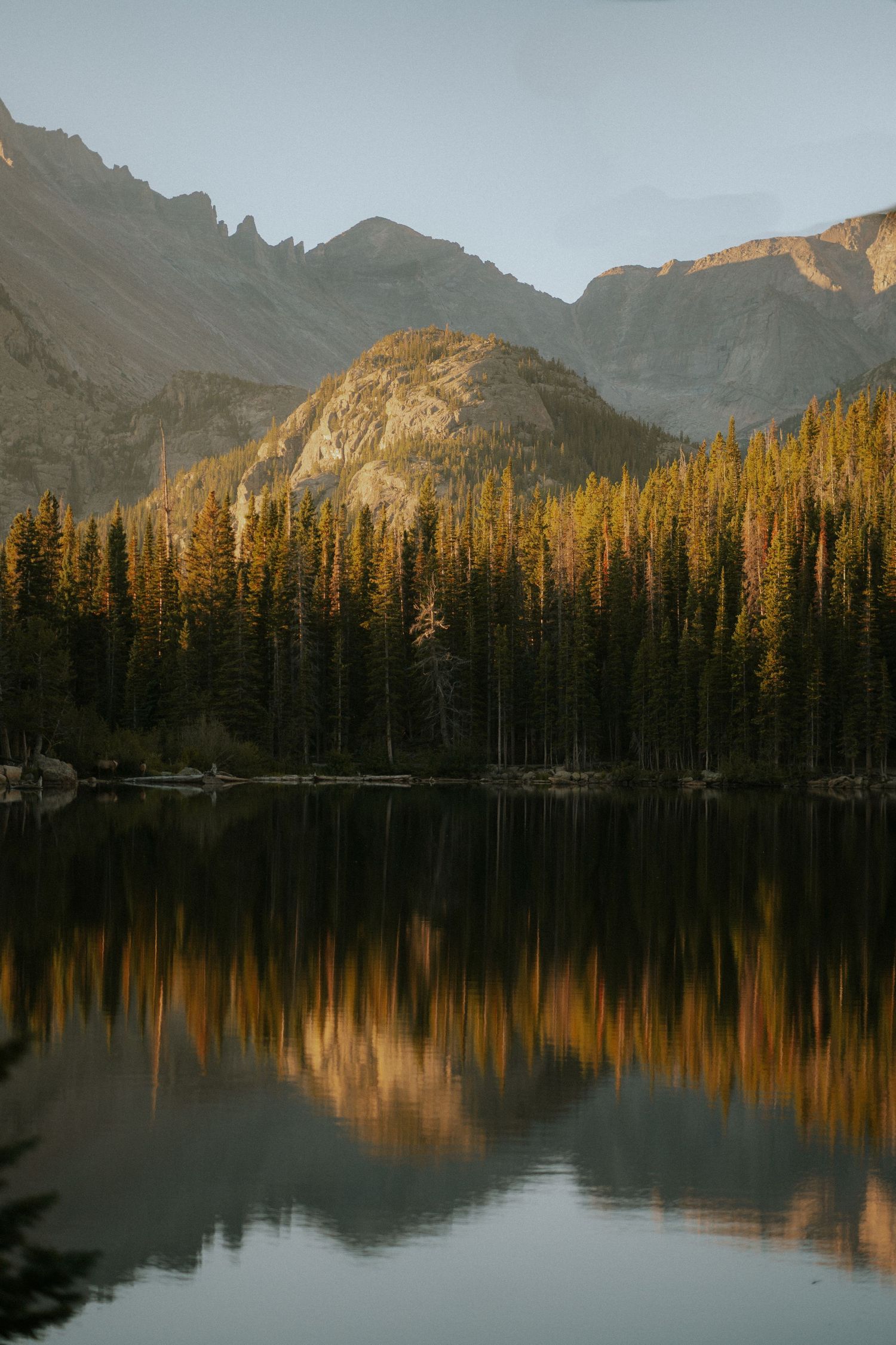 Serene mountain lake at sunset with evergreen forest and peaks reflected in still waters.