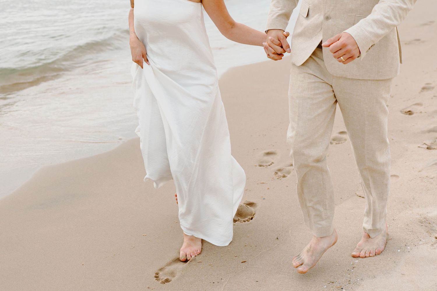 Couple's feet walking barefoot together on a sandy beach leaving footprints in their wake.