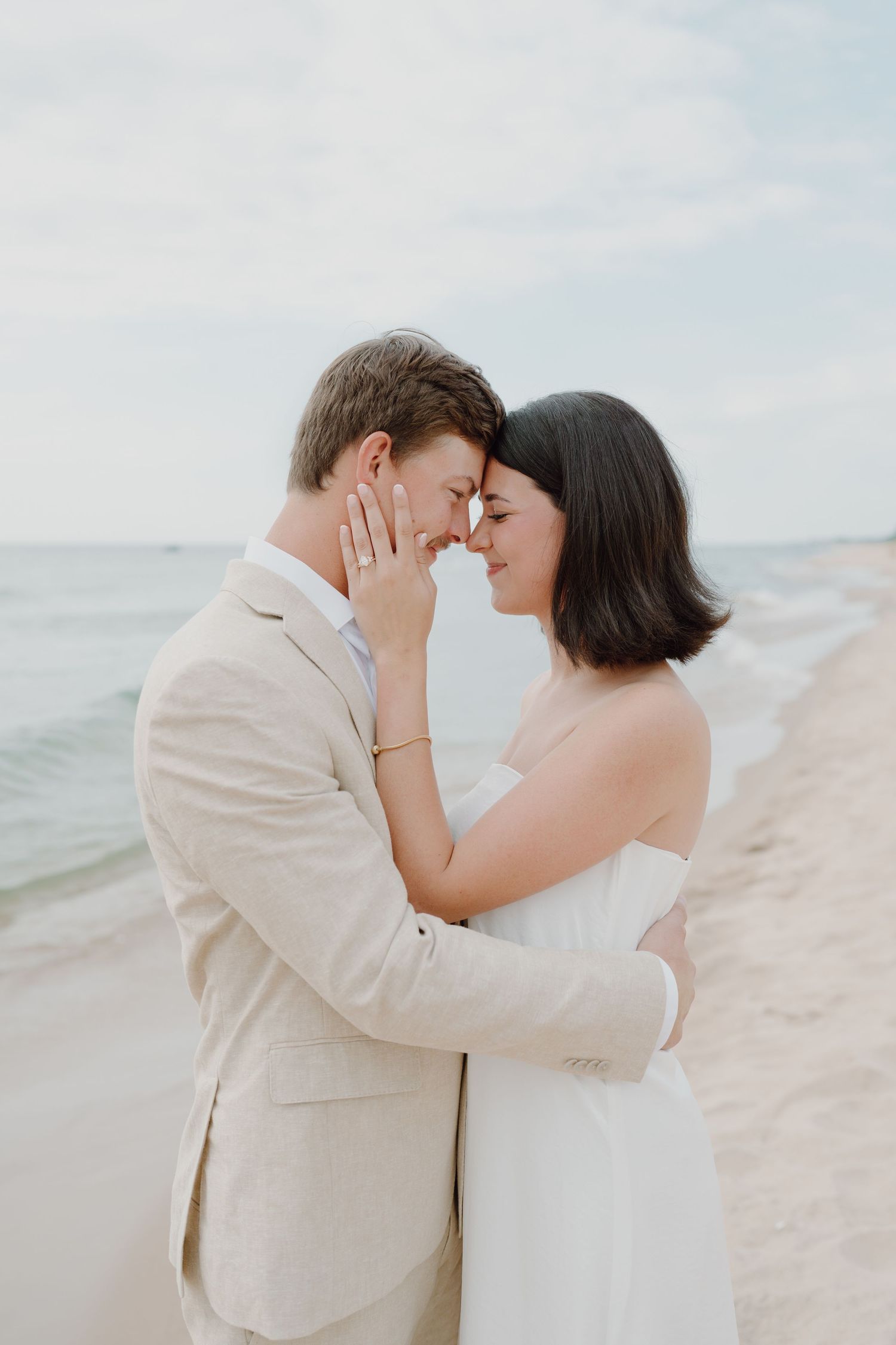 An intimate moment between a couple on a beach as they embrace with the ocean behind them.