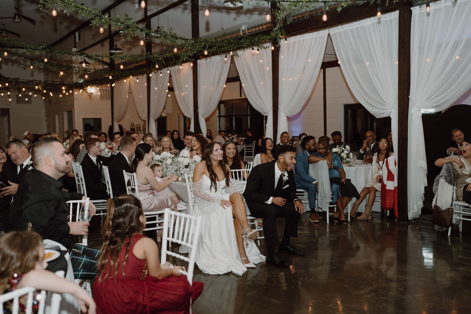 Wedding celebration in a rustic-modern venue with string lights and greenery decorations.