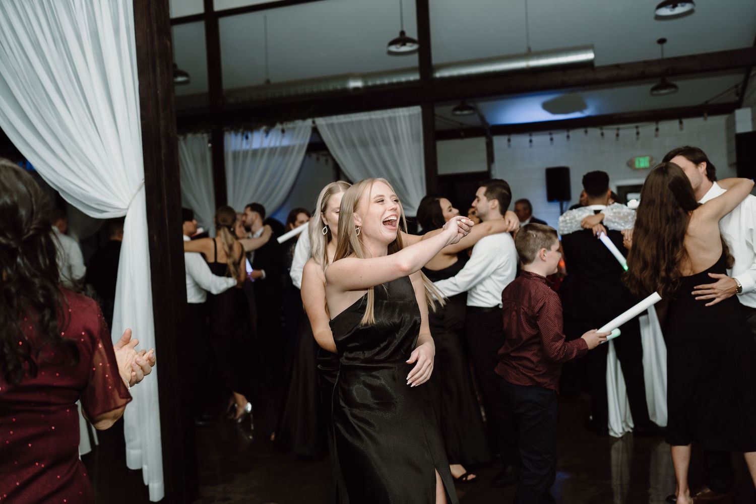 Wedding guests dancing enthusiastically at an indoor reception venue.