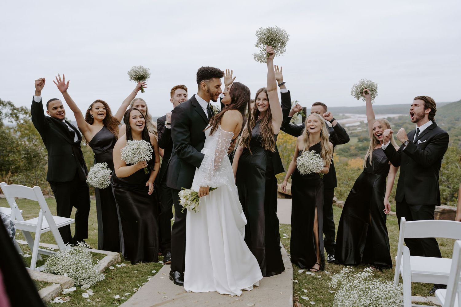 Wedding party celebrates with raised arms and cheers in an outdoor ceremony setting.
