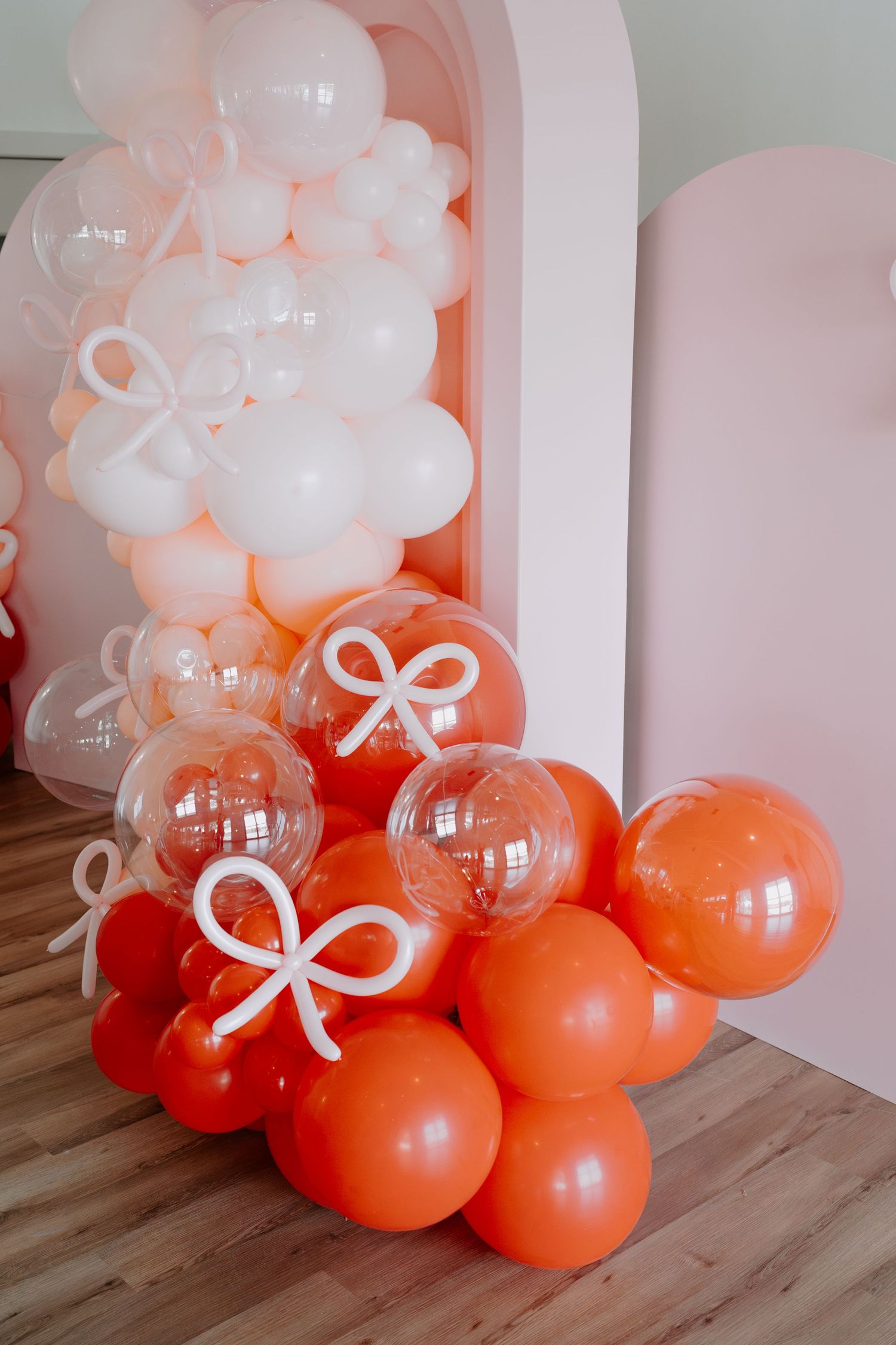 Red and orange balloon decorations arranged against a white wall with bow details.