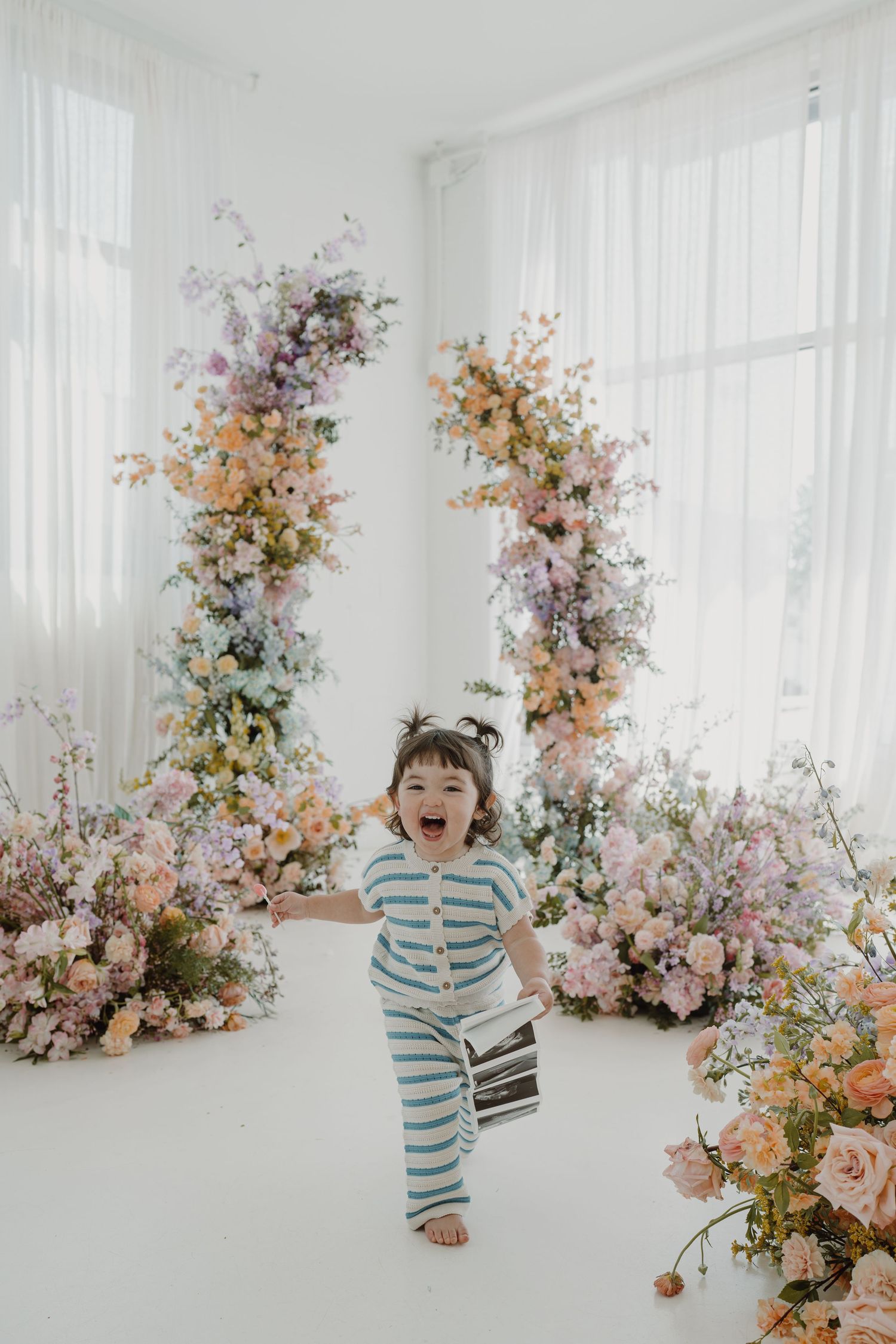 A joyful moment captured in a bright white studio with delicate floral arrangements in pink and peach tones.