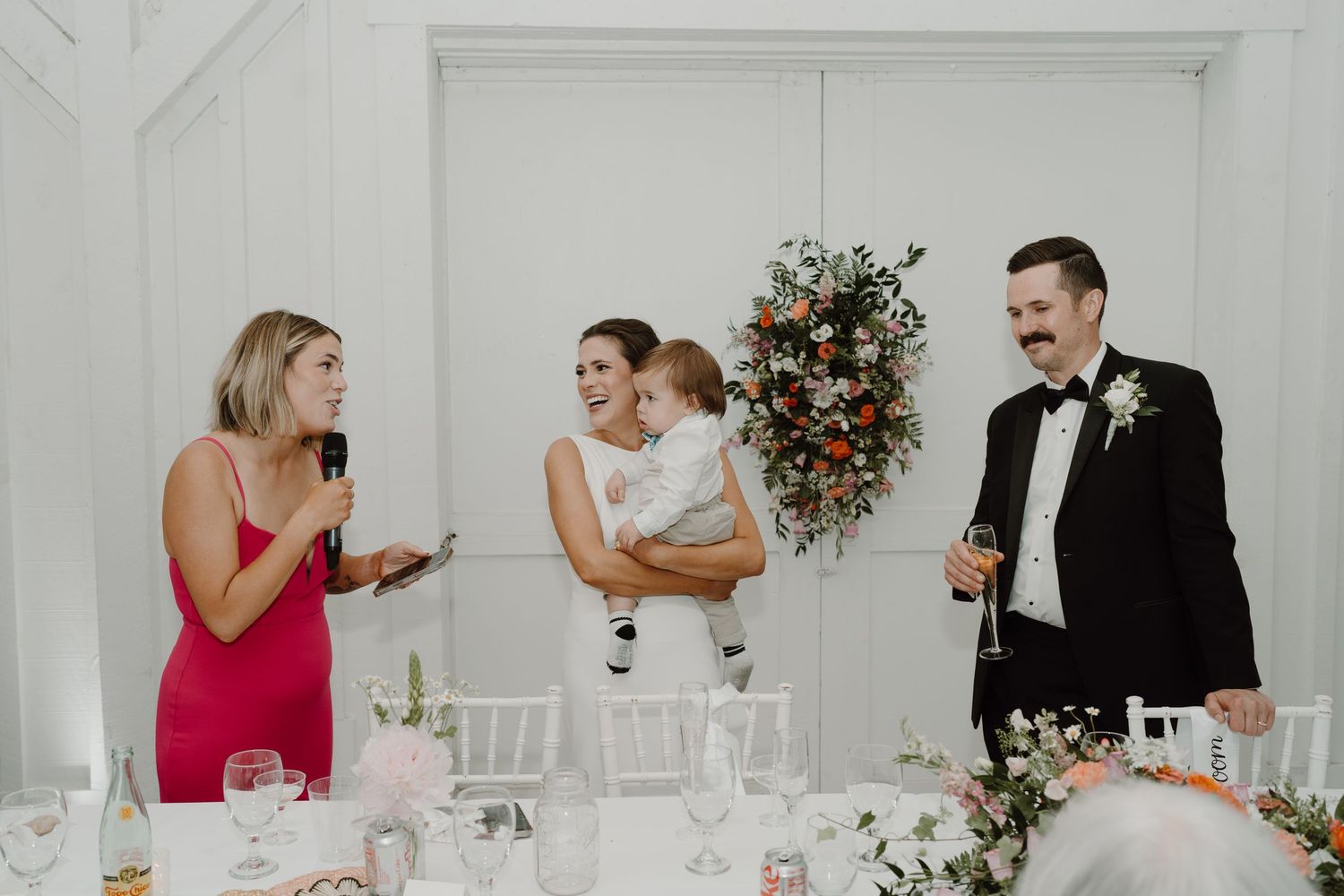 Wedding party members interacting during reception in a bright white venue.