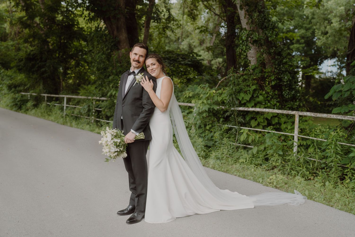Wedding couple walking along path with scenic lake view and greenery.