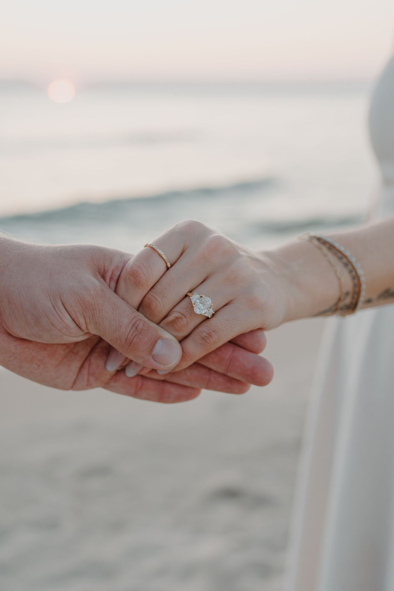 Close-up shots of hands holding and displaying an engagement ring on the beach.