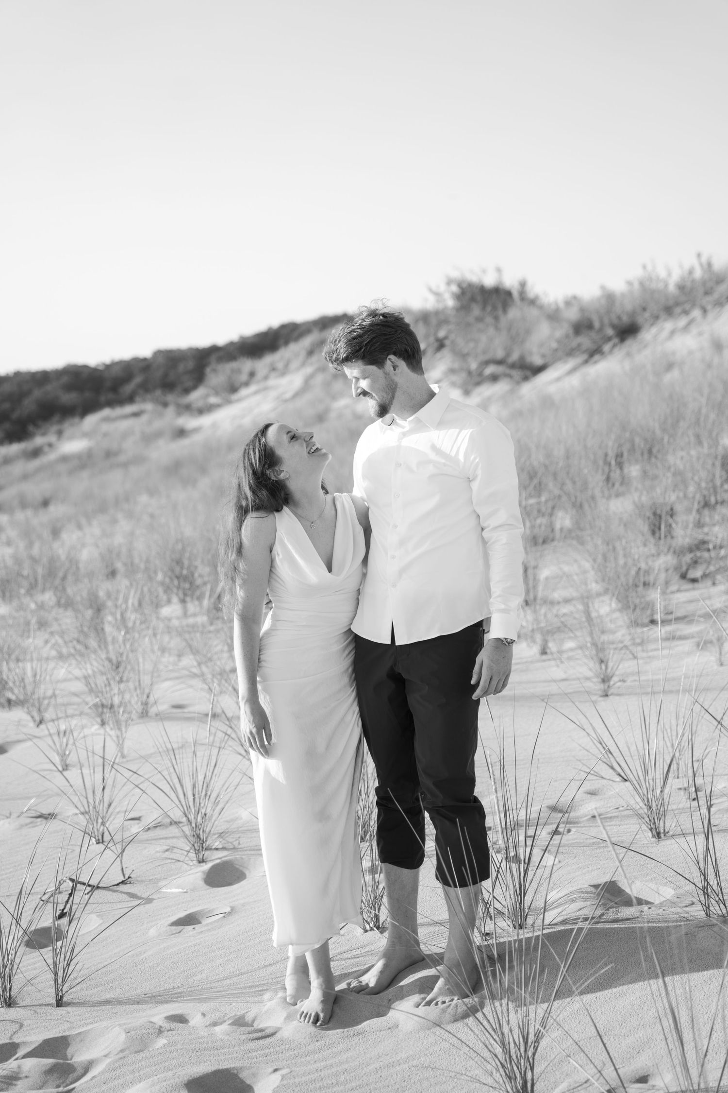 A romantic moment captured between two people on sandy dunes at the beach.
