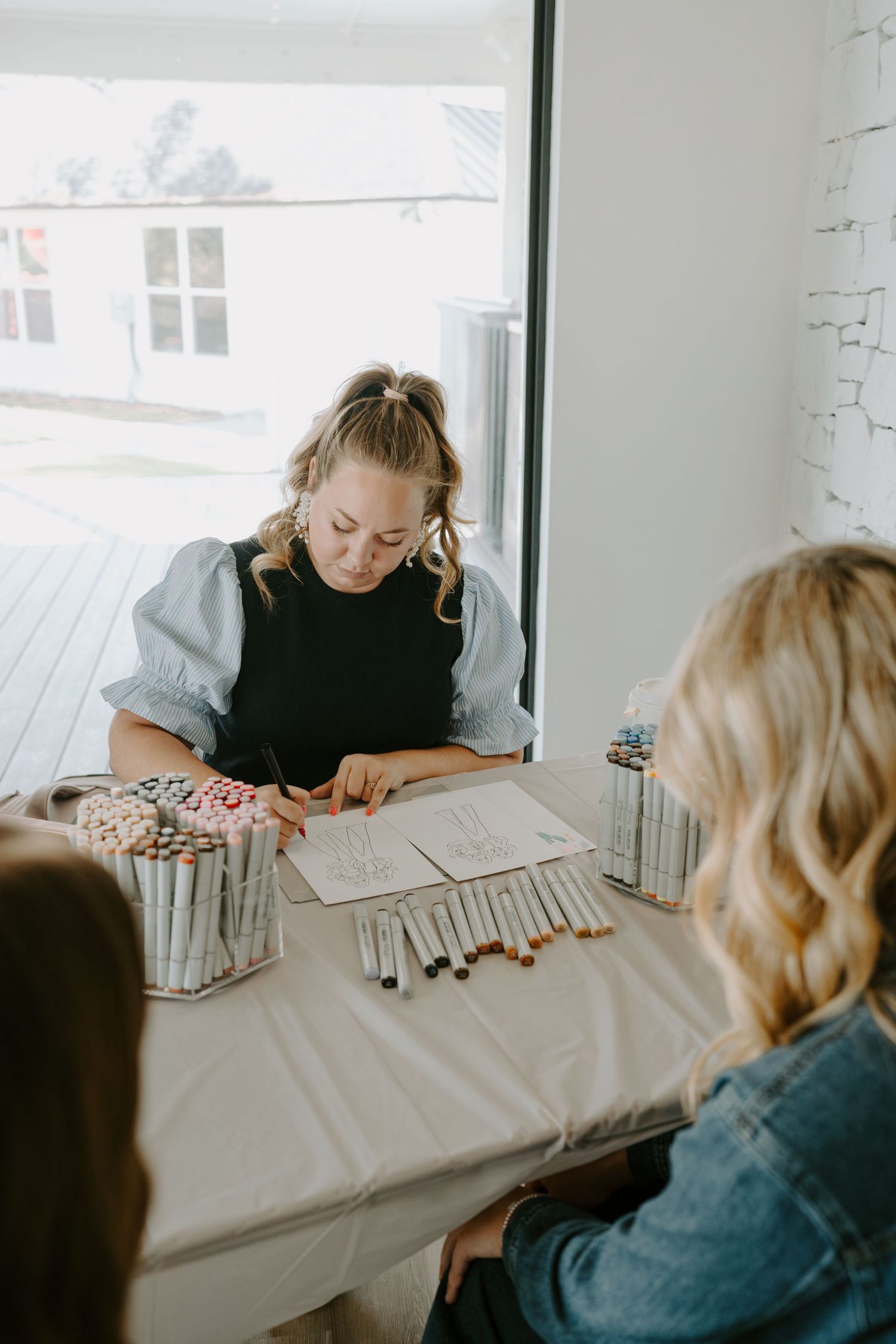 Someone working on creative materials at a white table near a bright window.
