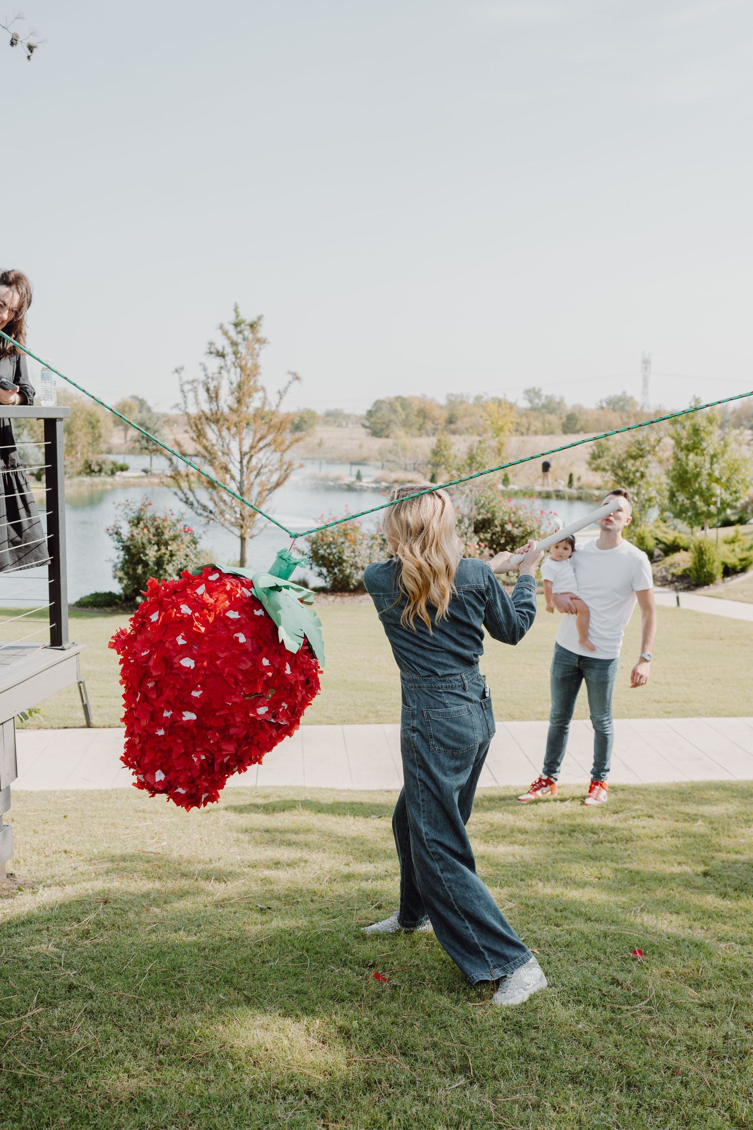 A person in denim swings a bright red heart piñata outdoors.