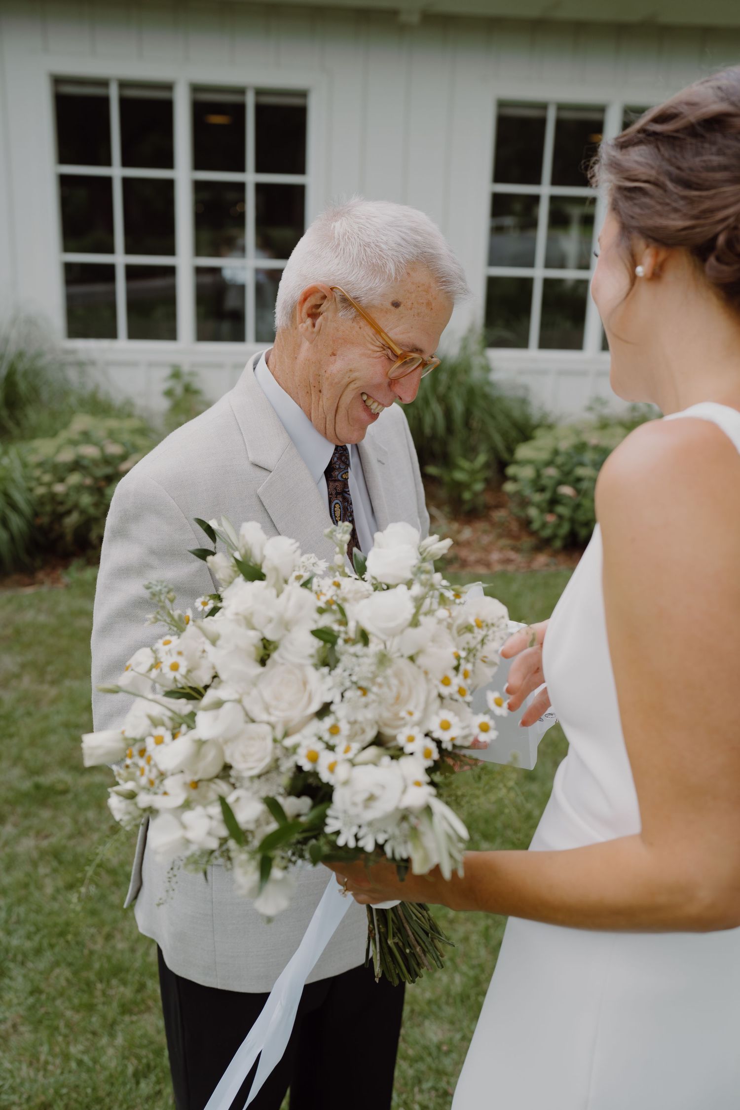 A heartwarming wedding moment captured outdoors with white flowers and a white dress against a building backdrop.