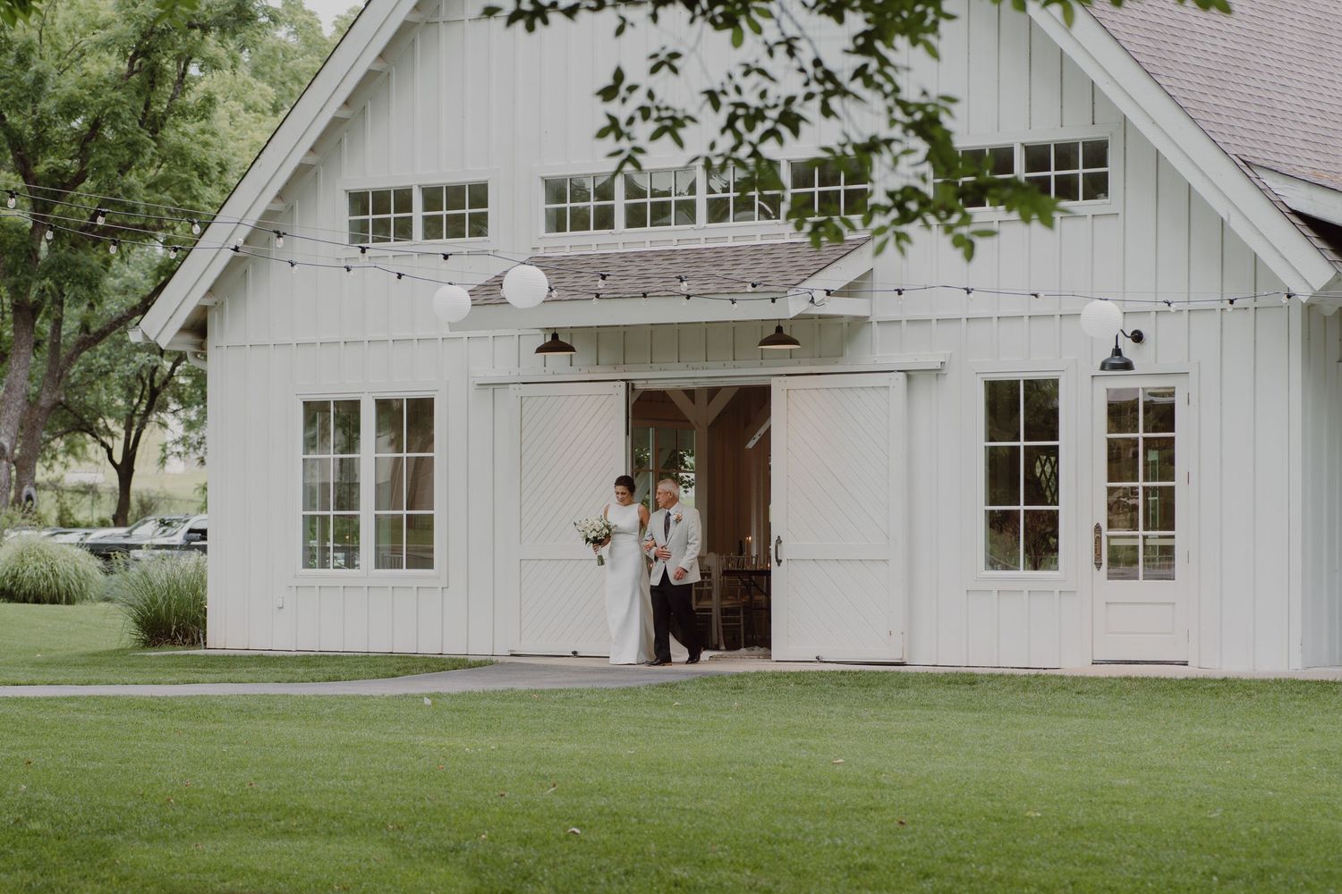 White barn-style wedding venue with multiple windows and string lights visible.
