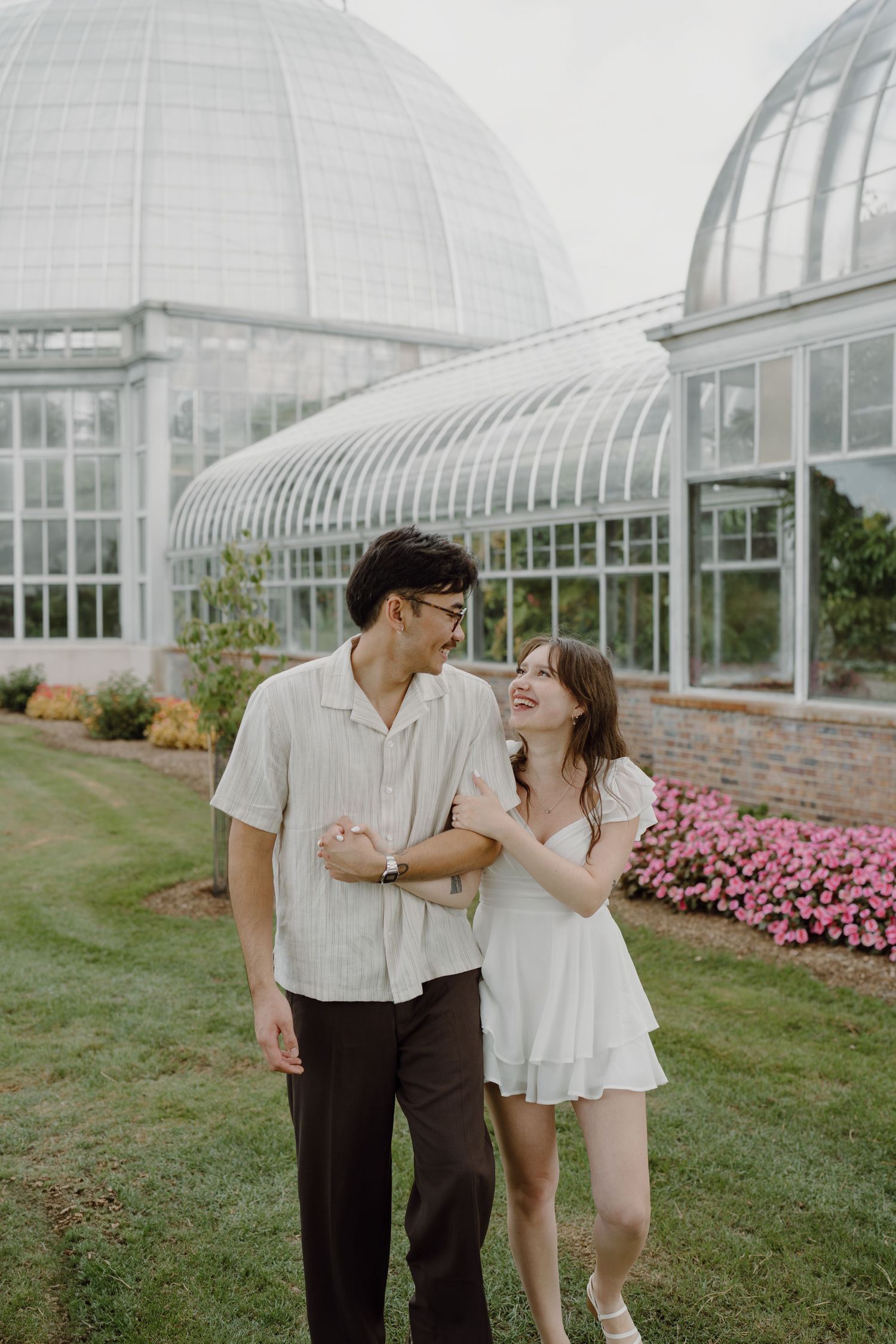 Two people laugh together during a photo session outside a domed conservatory building.