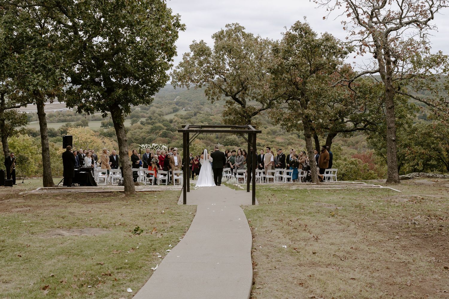 Scenic outdoor wedding ceremony setup with white chairs and floral arrangements on a hilltop overlooking a valley.