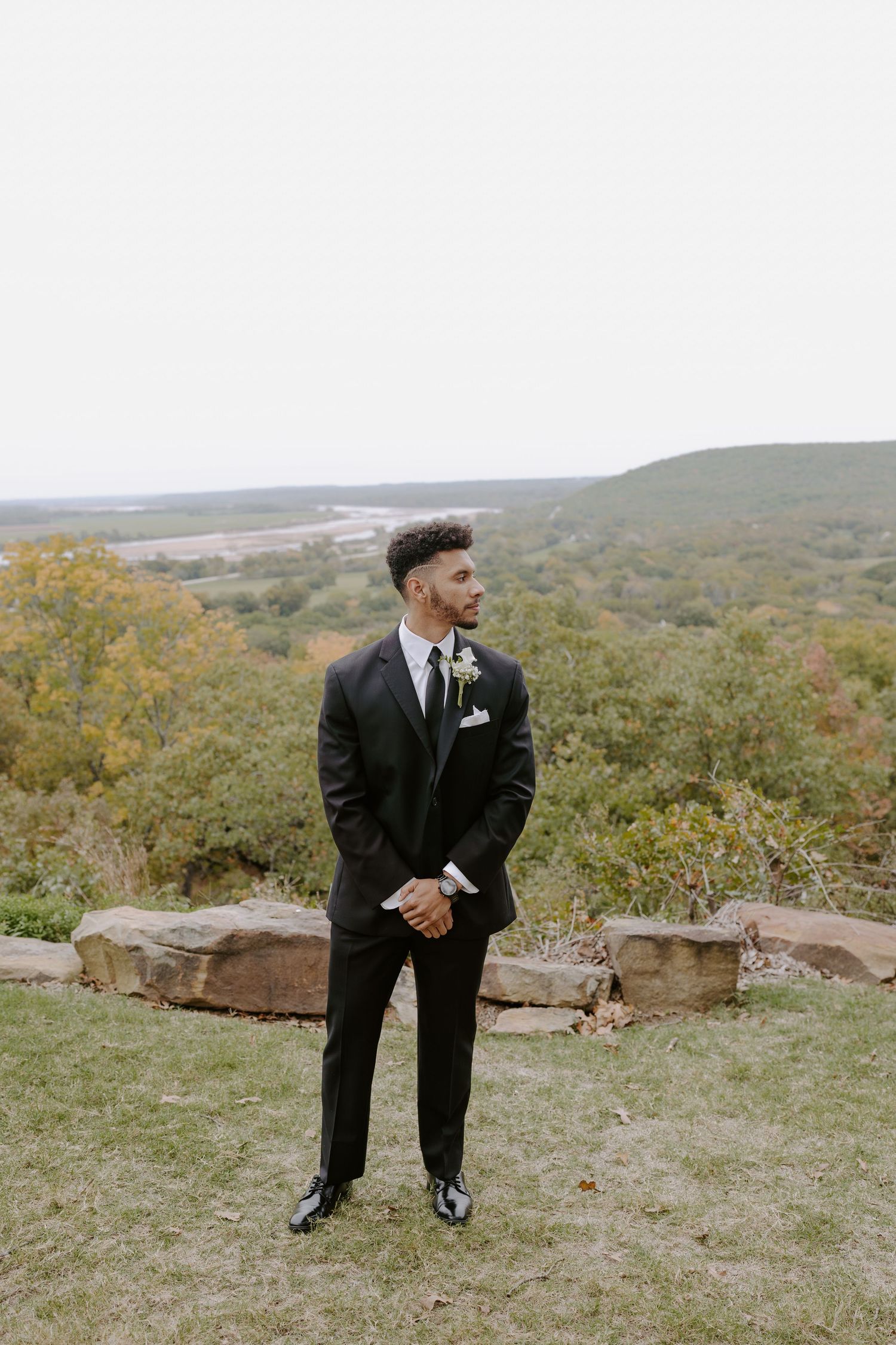 Person in formal attire stands alone on grassy hilltop during wedding photo session.