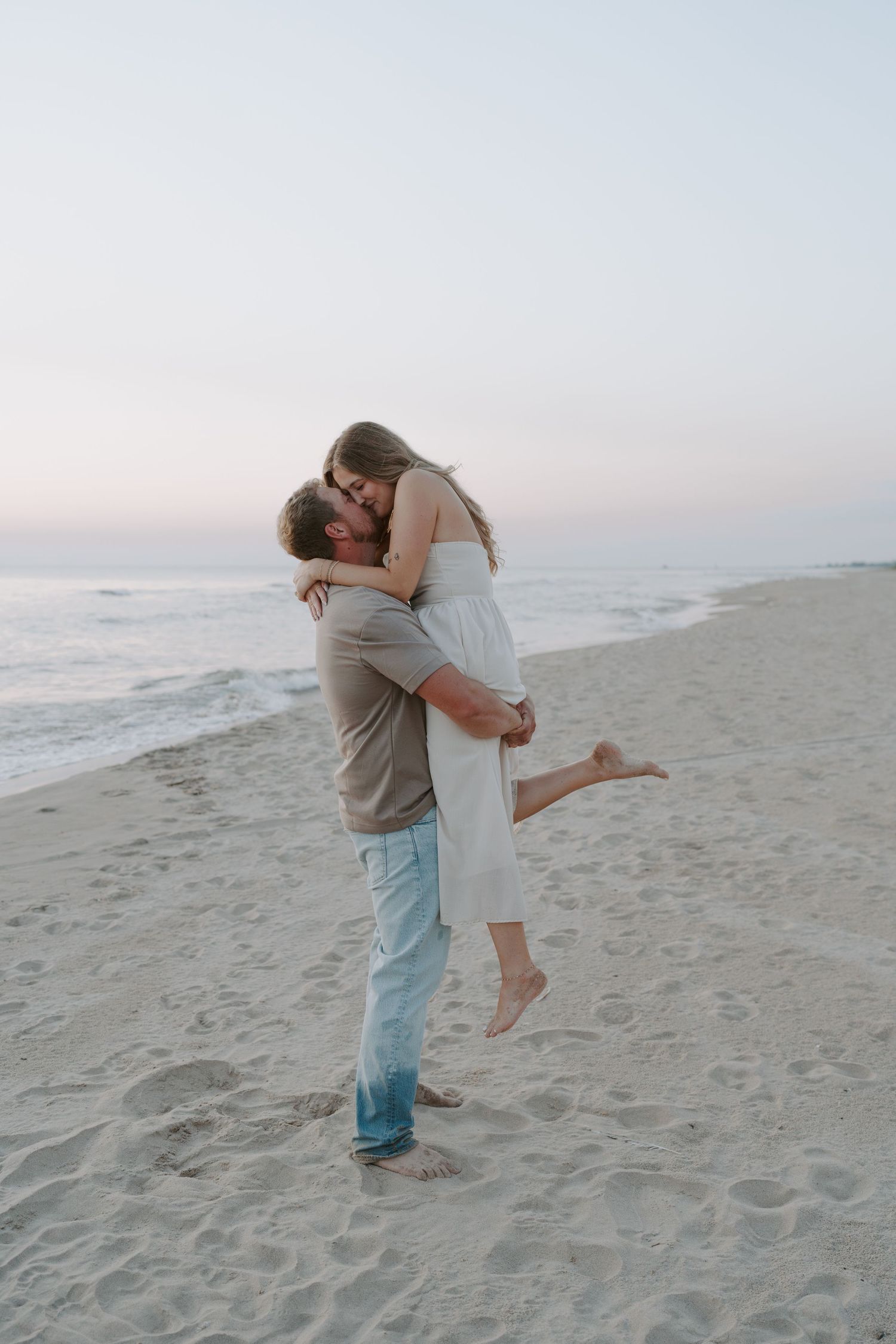 Couple in casual attire sharing romantic lifts and embraces by the ocean.
