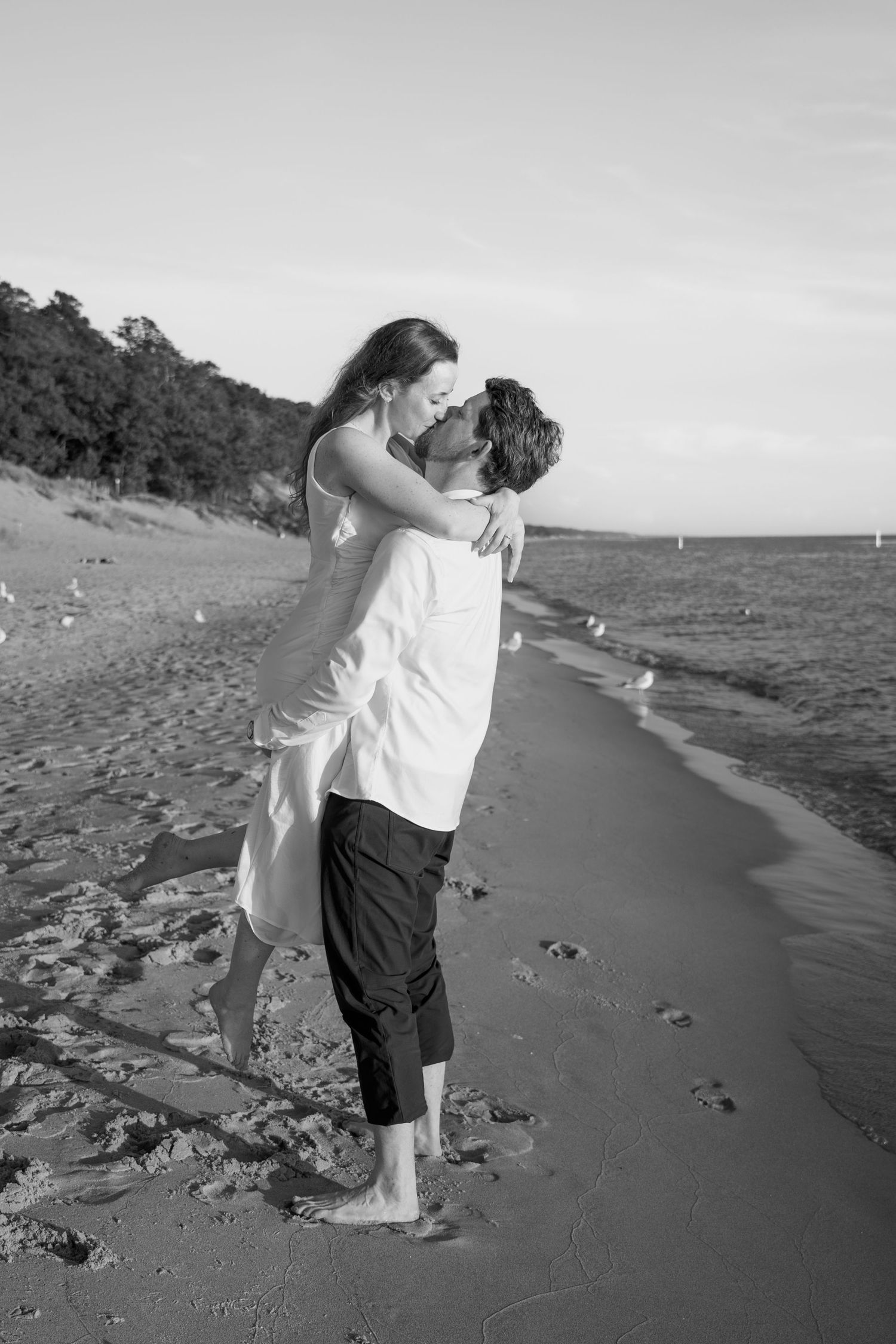 Black and white photos of couple embracing on beach shoreline.