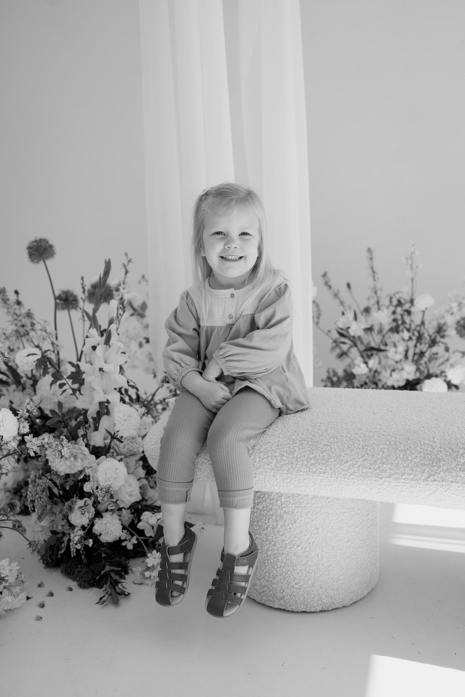 Child sitting on a white ottoman surrounded by delicate floral arrangements in black and white.