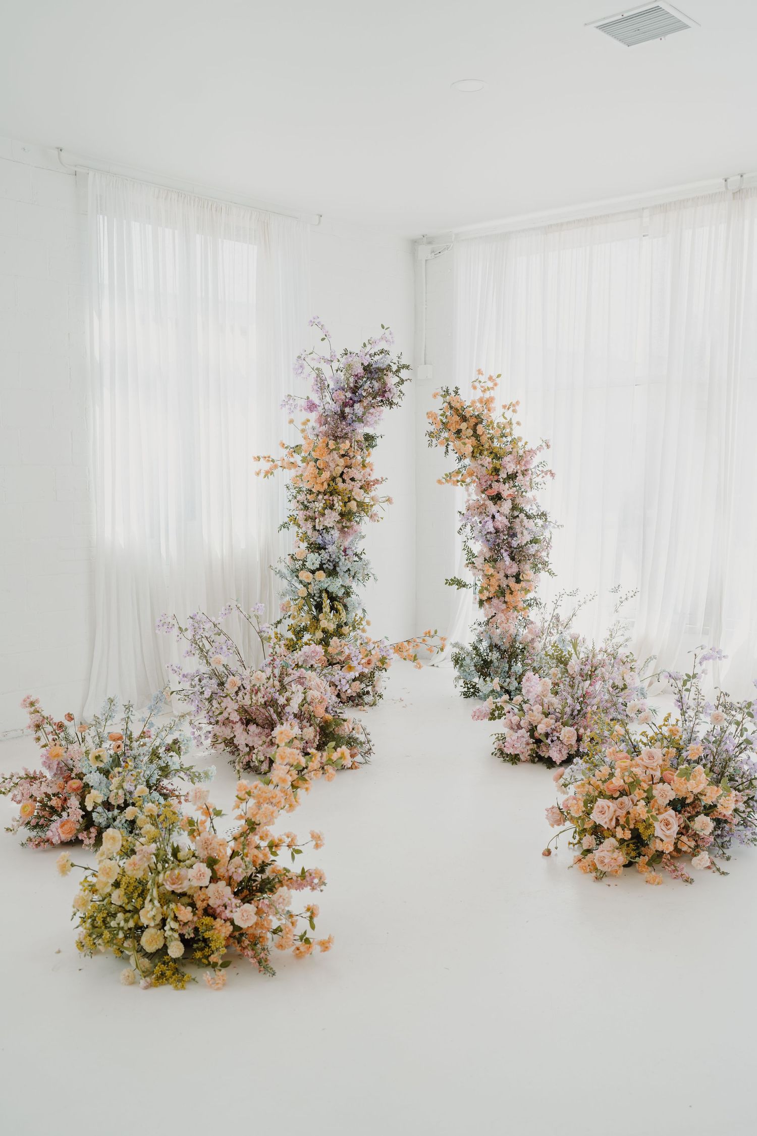 Beautiful floral arch installation with pink and peach blooms in white studio space.