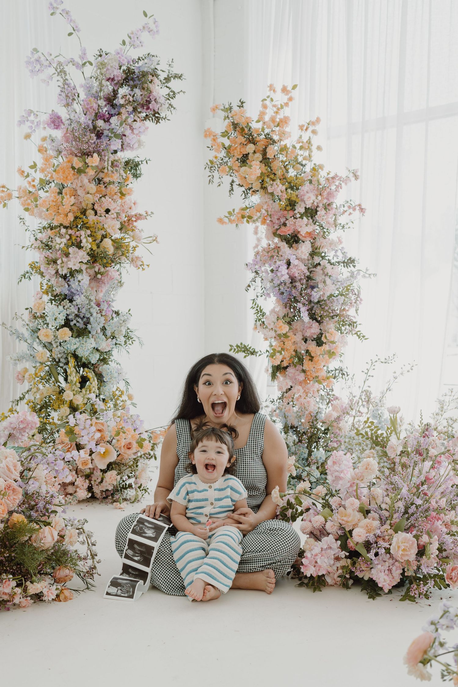 Joyful family photoshoot in a bright white studio with beautiful floral arrangements in pink and peach tones.