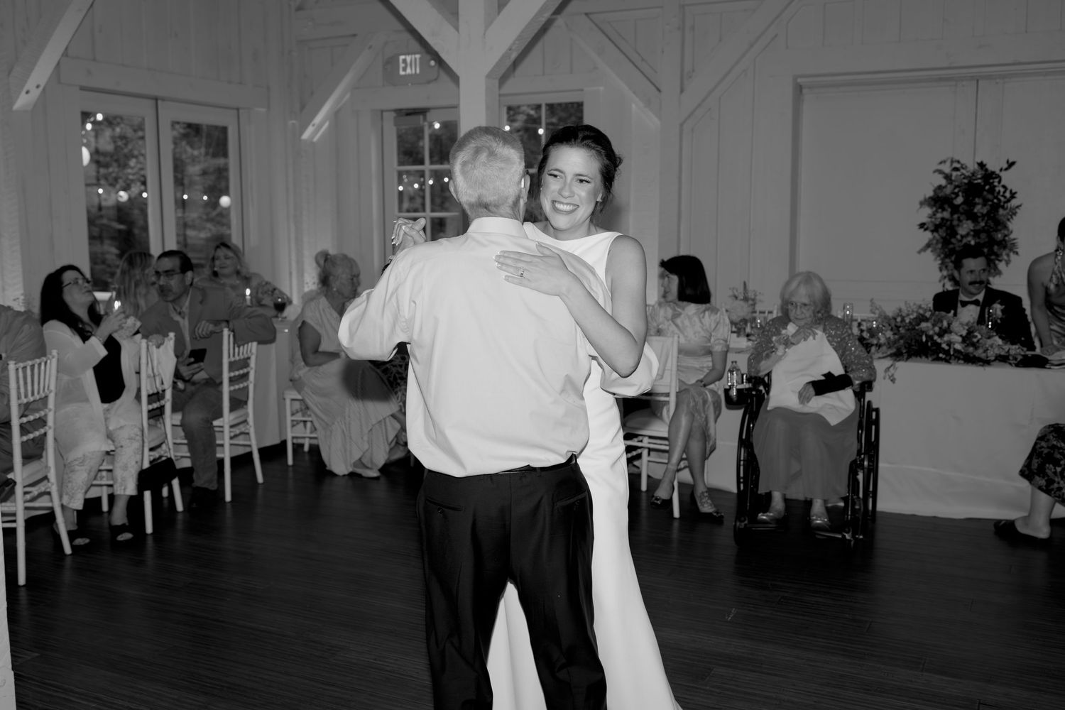 Black and white photo of a dance in a rustic barn venue with guests seated at tables.