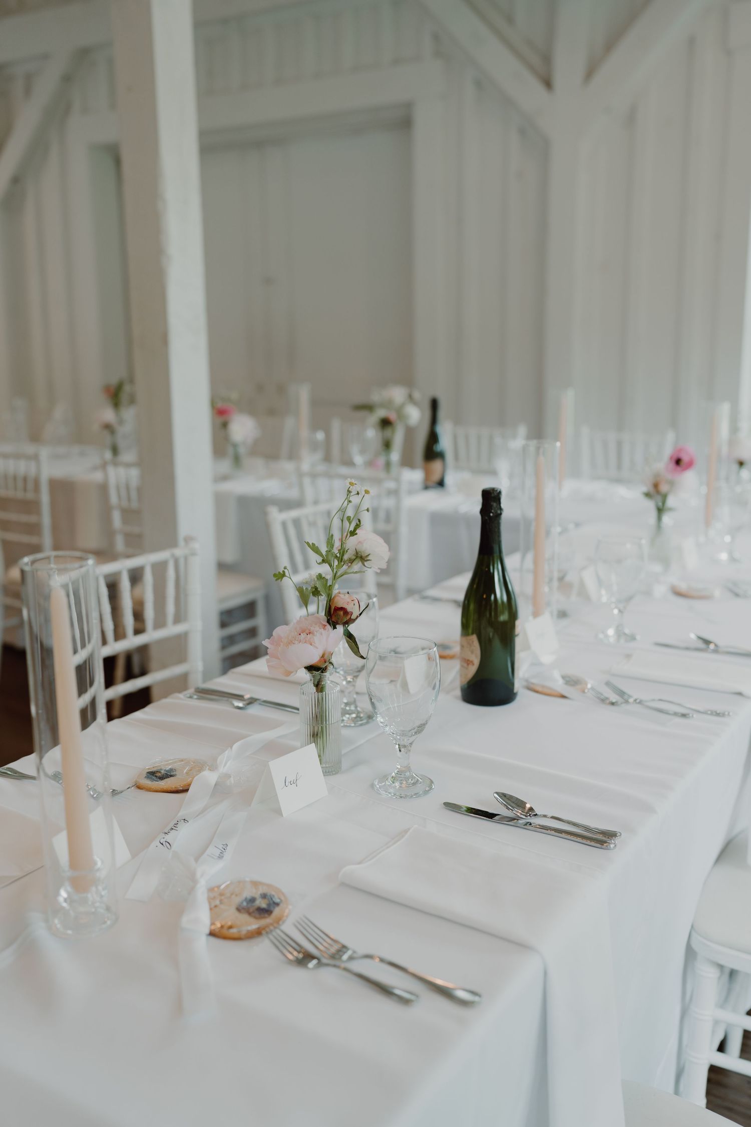 White reception tables set with crisp linens, wine glasses and simple floral arrangements.