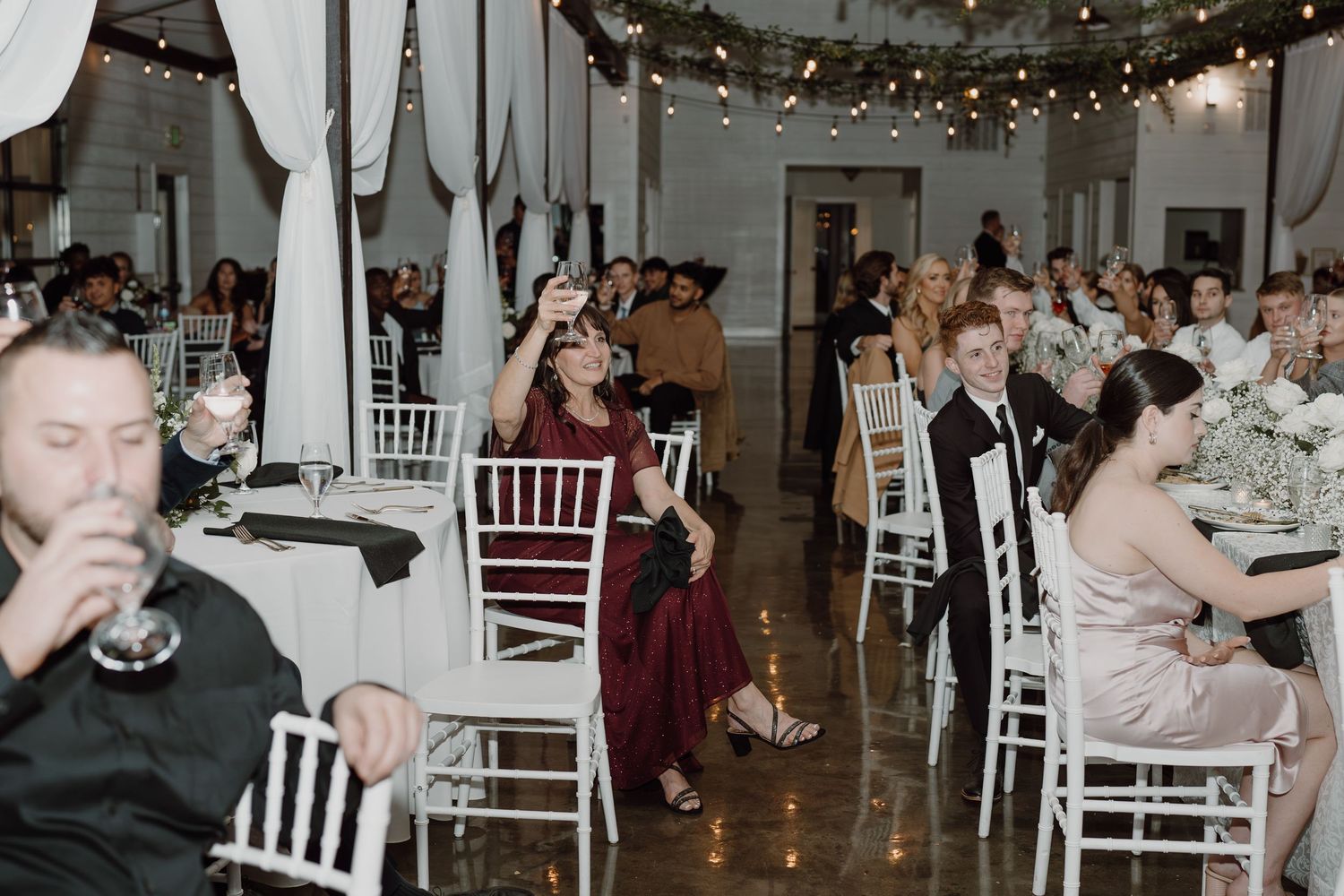 Wedding guests dance and celebrate on the reception dance floor under string lights and white decor.