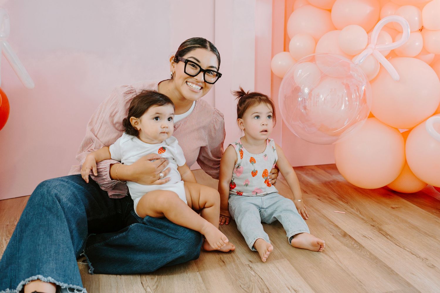 Family photo session with pink balloon decorations and hardwood floors.