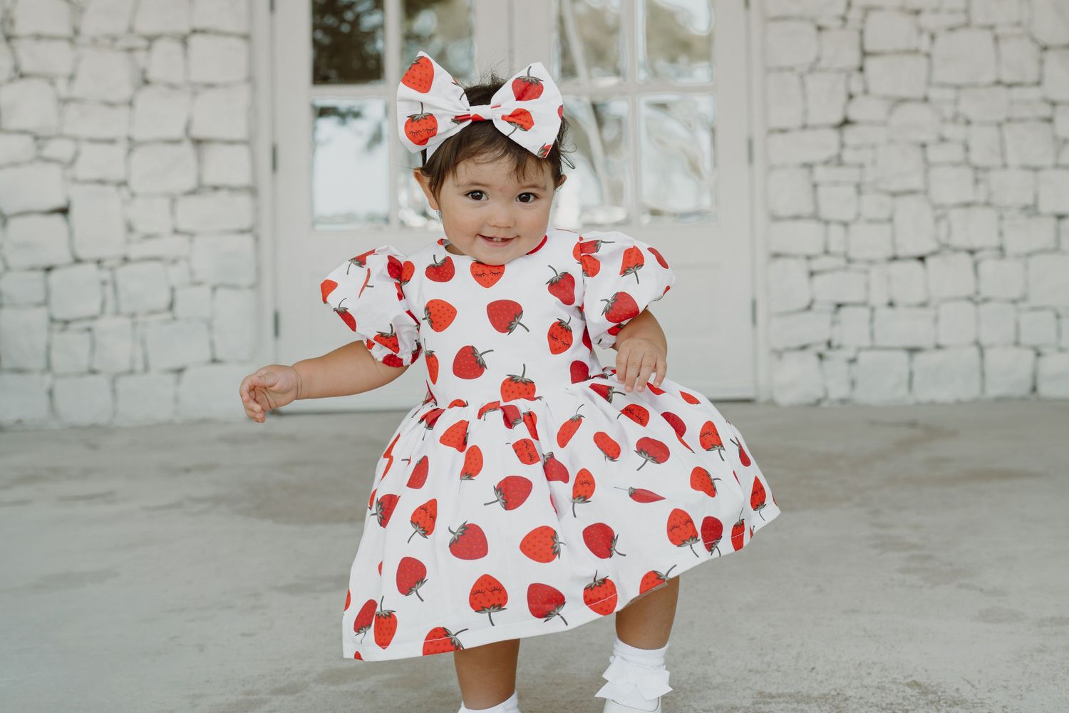 Spinning and dancing in red heart-patterned dress against white stone wall.