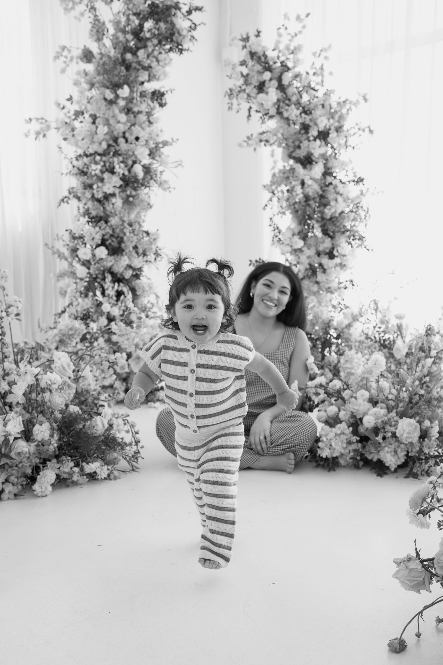 Black and white studio portrait showing playful moments against a floral backdrop.