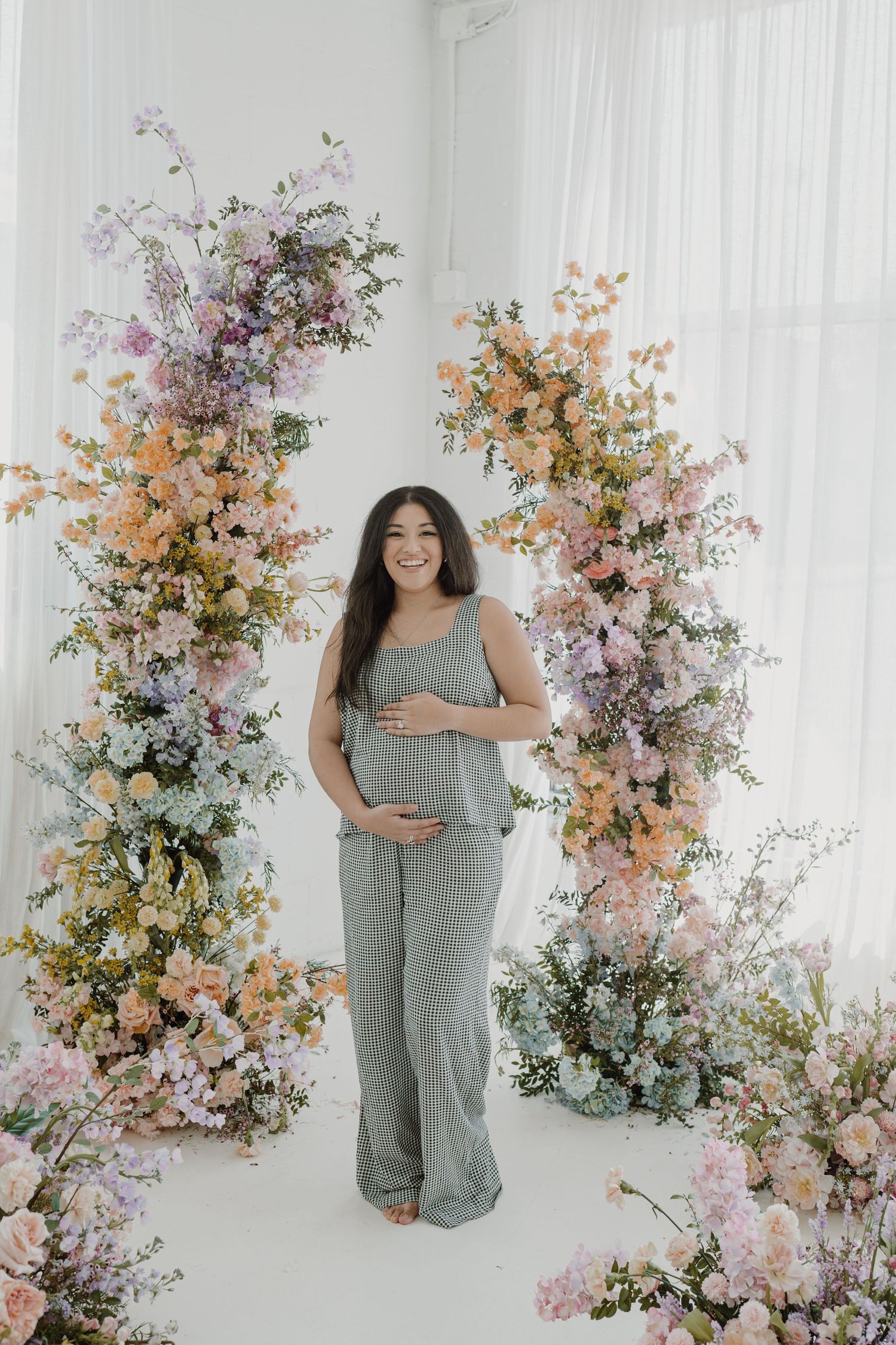 Maternity portraits in white studio with romantic floral arrangements in soft pink and peach tones.