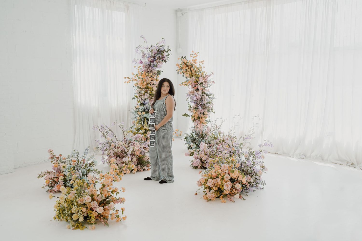 Woman in gray dress poses under romantic floral arch with mixed blooms.