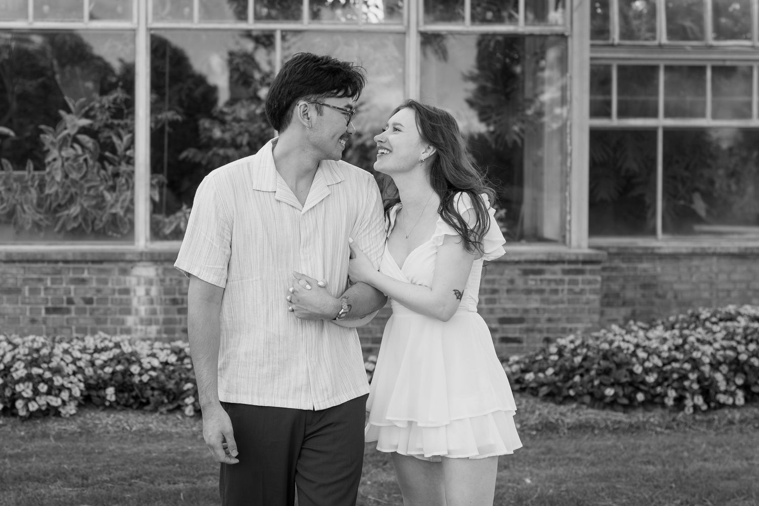 A couple enjoys a tender moment together outside a glass conservatory on a sunny day.