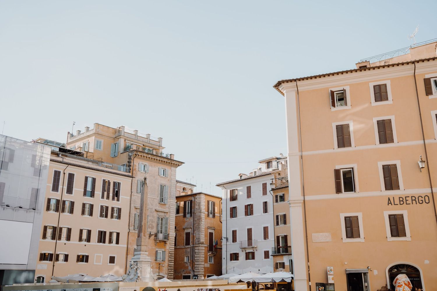 Historic Italian buildings with terracotta colored facades line a sunny square in Rome.