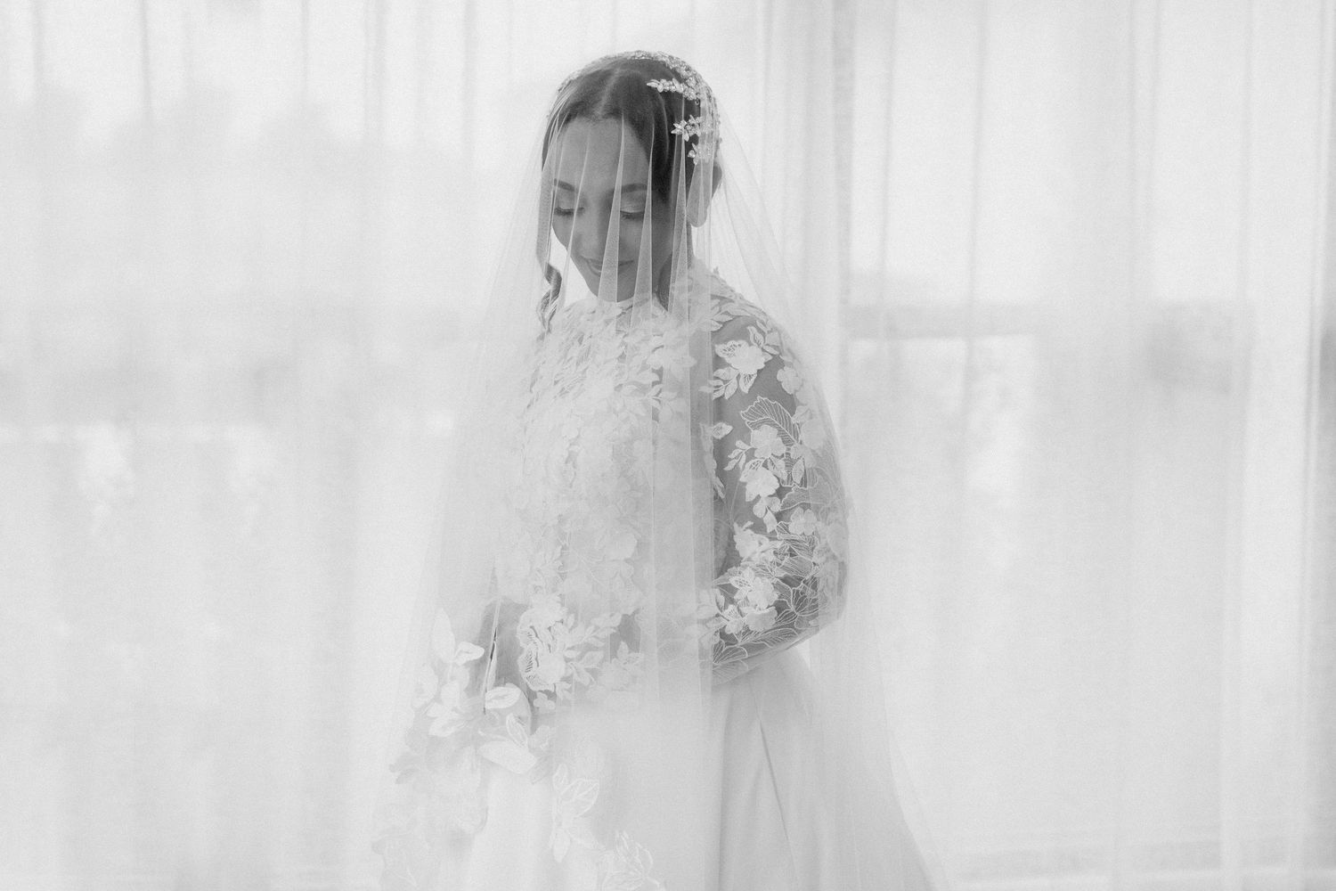 Ethereal bridal portrait with soft lighting and lace details through sheer curtains.