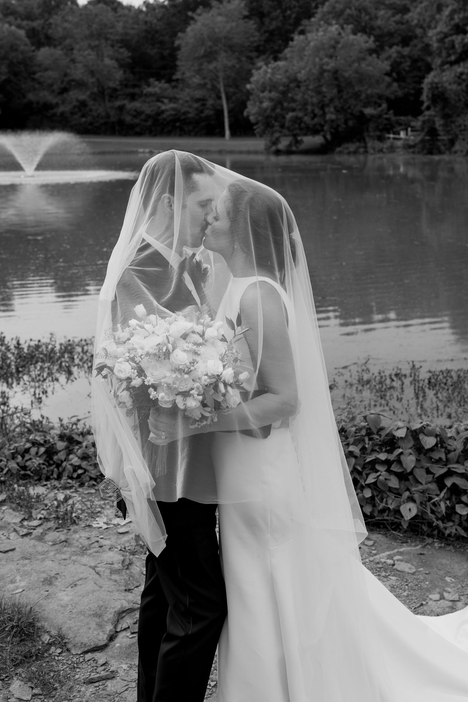 Elegant wedding portrait in black and white by waterfront with cascading veil.